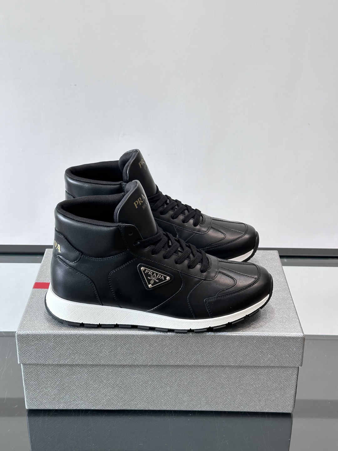 PRADA/普拉达 男士新款高帮运动鞋，这款厚底运动鞋采用牛皮鞋面制成，搭配加厚橡胶发泡中底拼接前后包裹