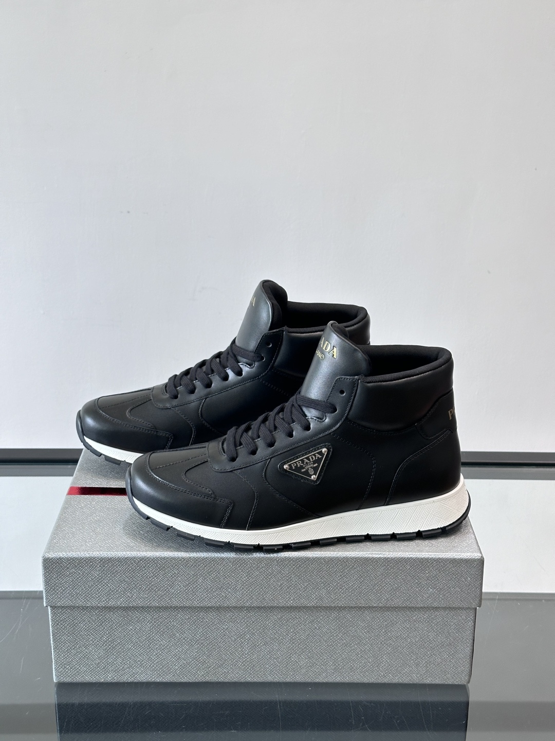 PRADA/普拉达 男士新款高帮运动鞋，这款厚底运动鞋采用牛皮鞋面制成，搭配加厚橡胶发泡中底拼接前后包裹