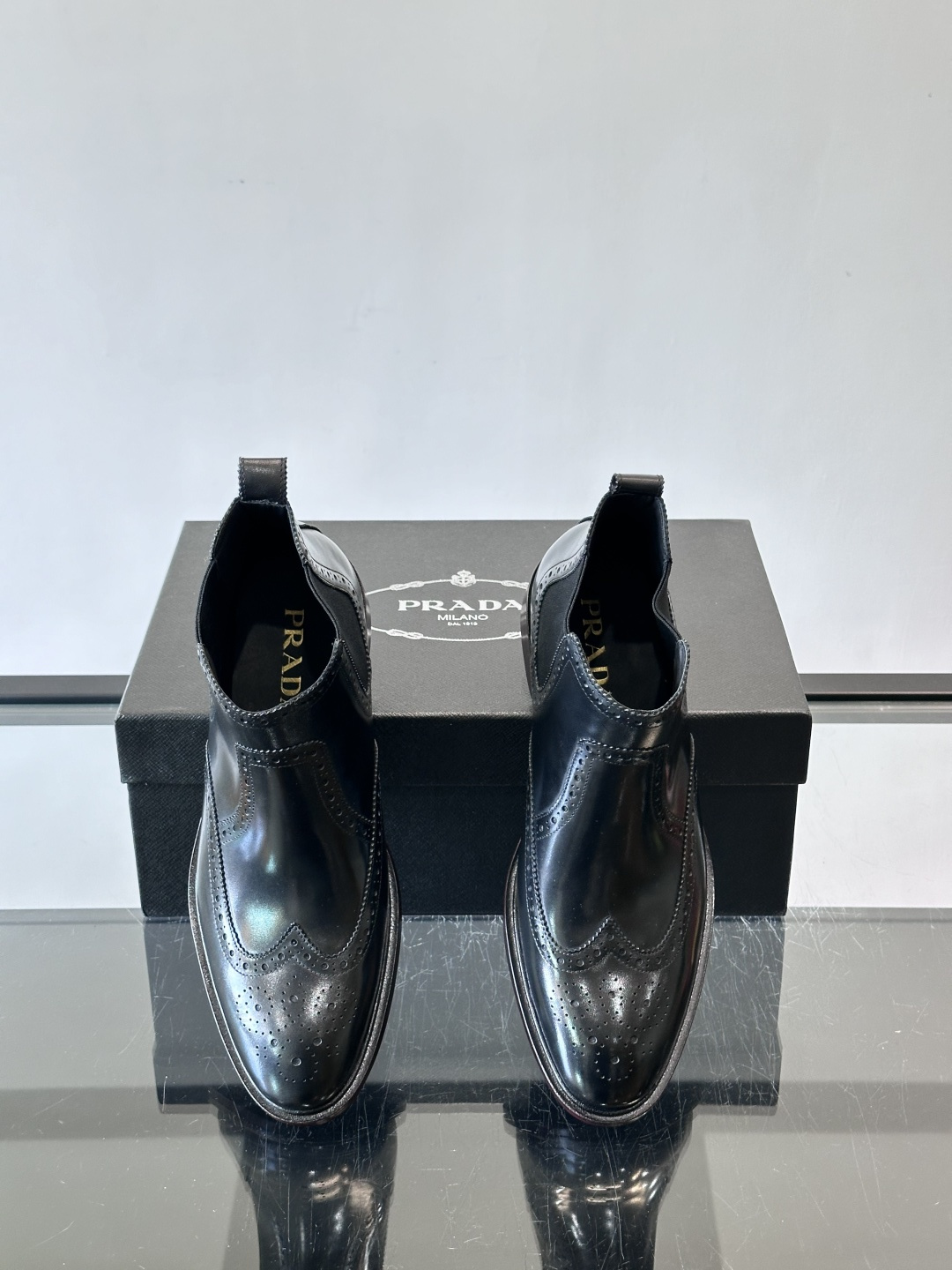 Prada普拉达布洛克雕花切尔西靴，英伦风代表，采用高光抛光皮革，光泽感如黑曜石。鞋面布洛克雕花，细节精