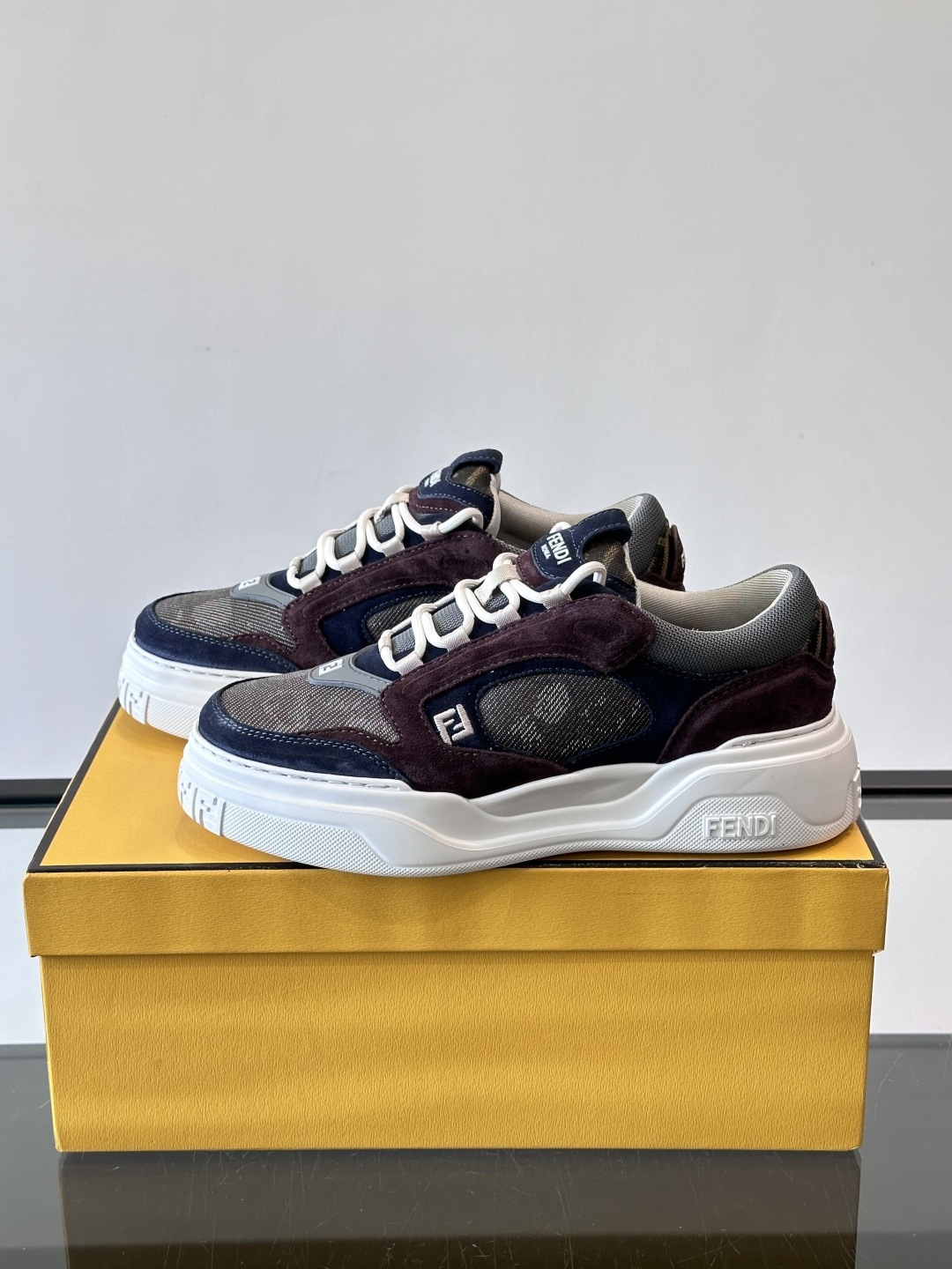 FENDI男士老爹鞋采用深紫、藏蓝与灰色拼接设计，麂皮与网眼材质混搭，厚底白色中底印有品牌Logo，整体