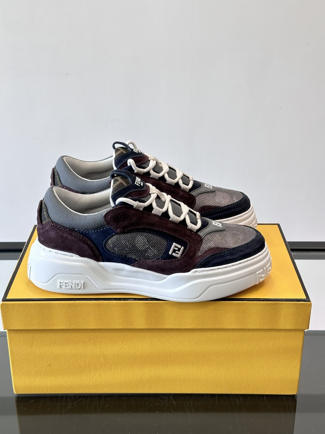 FENDI男士老爹鞋采用深紫、藏蓝与灰色拼接设计，麂皮与网眼材质混搭，厚底白色中底印有品牌Logo，整体