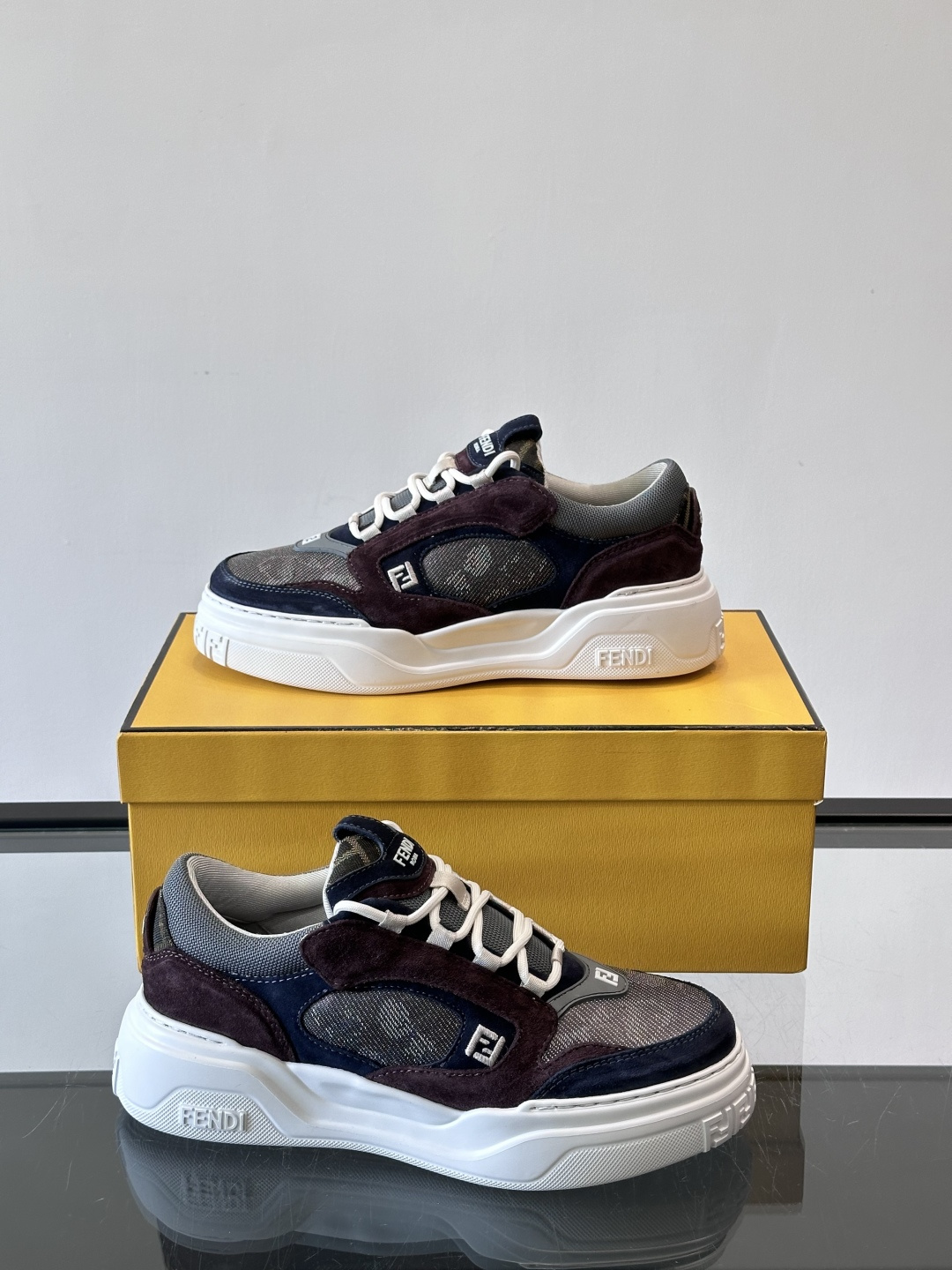 FENDI男士老爹鞋采用深紫、藏蓝与灰色拼接设计，麂皮与网眼材质混搭，厚底白色中底印有品牌Logo，整体