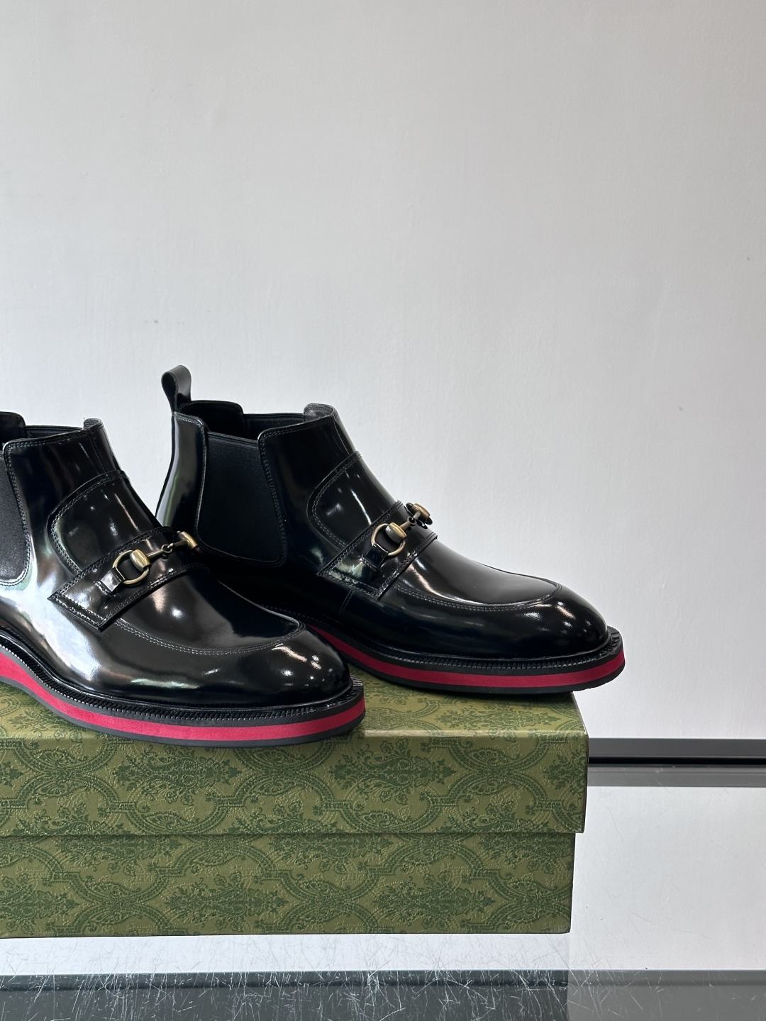 Gucci经典的拼色切尔西靴，采用高光泽黑色皮革搭配标志性的红绿织带细节，鞋底为亮眼的红色，整体设计兼具