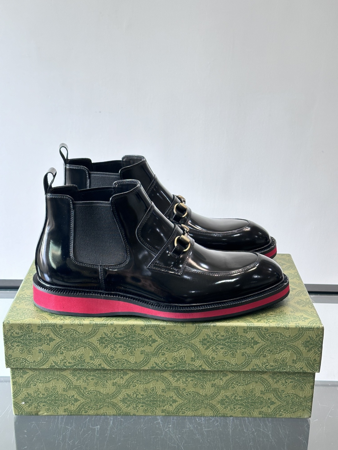 Gucci经典的拼色切尔西靴，采用高光泽黑色皮革搭配标志性的红绿织带细节，鞋底为亮眼的红色，整体设计兼具