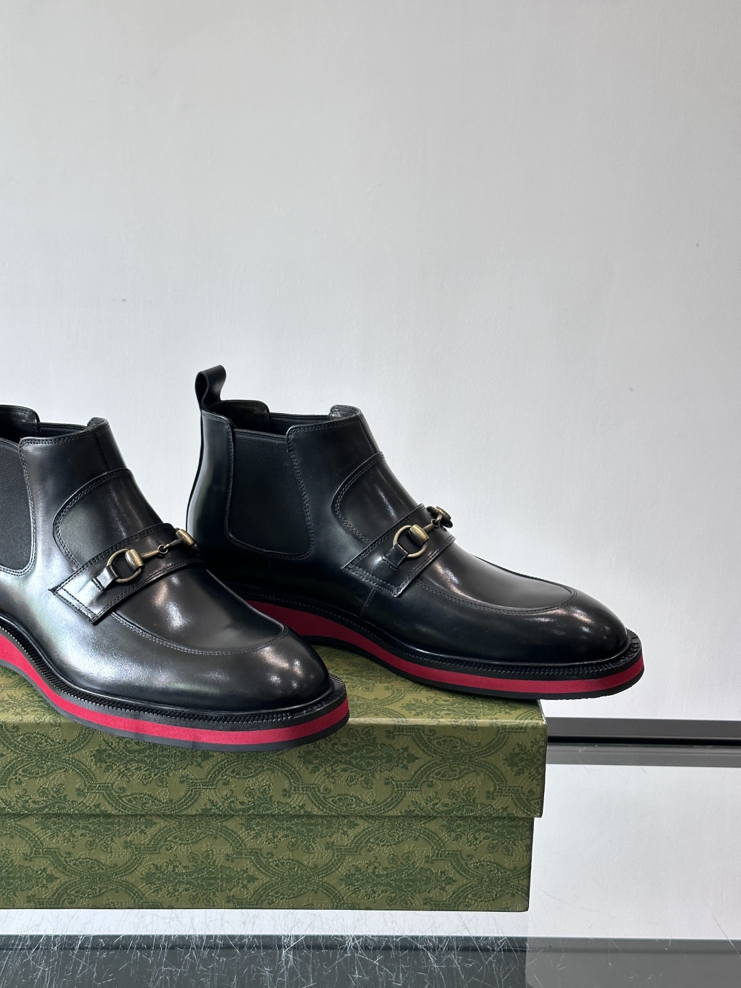 Gucci经典的拼色切尔西靴，采用高光泽黑色皮革搭配标志性的红绿织带细节，鞋底为亮眼的红色，整体设计兼具