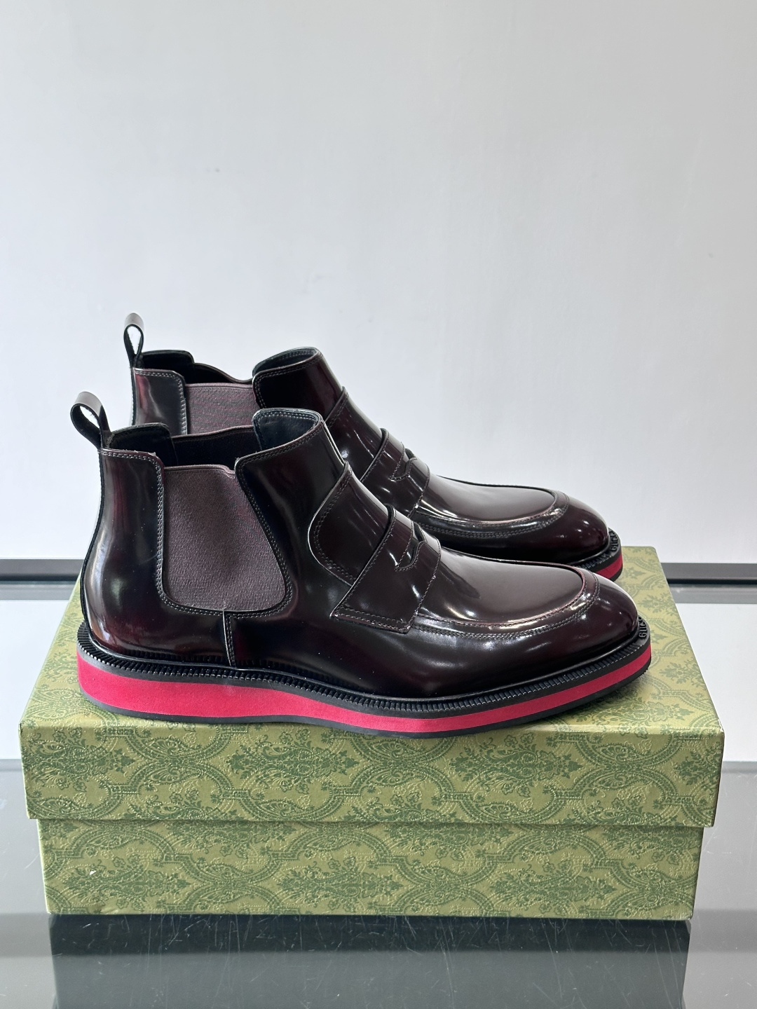 Gucci经典的拼色切尔西靴，采用高光泽黑色皮革搭配标志性的红绿织带细节，鞋底为亮眼的红色，整体设计兼具