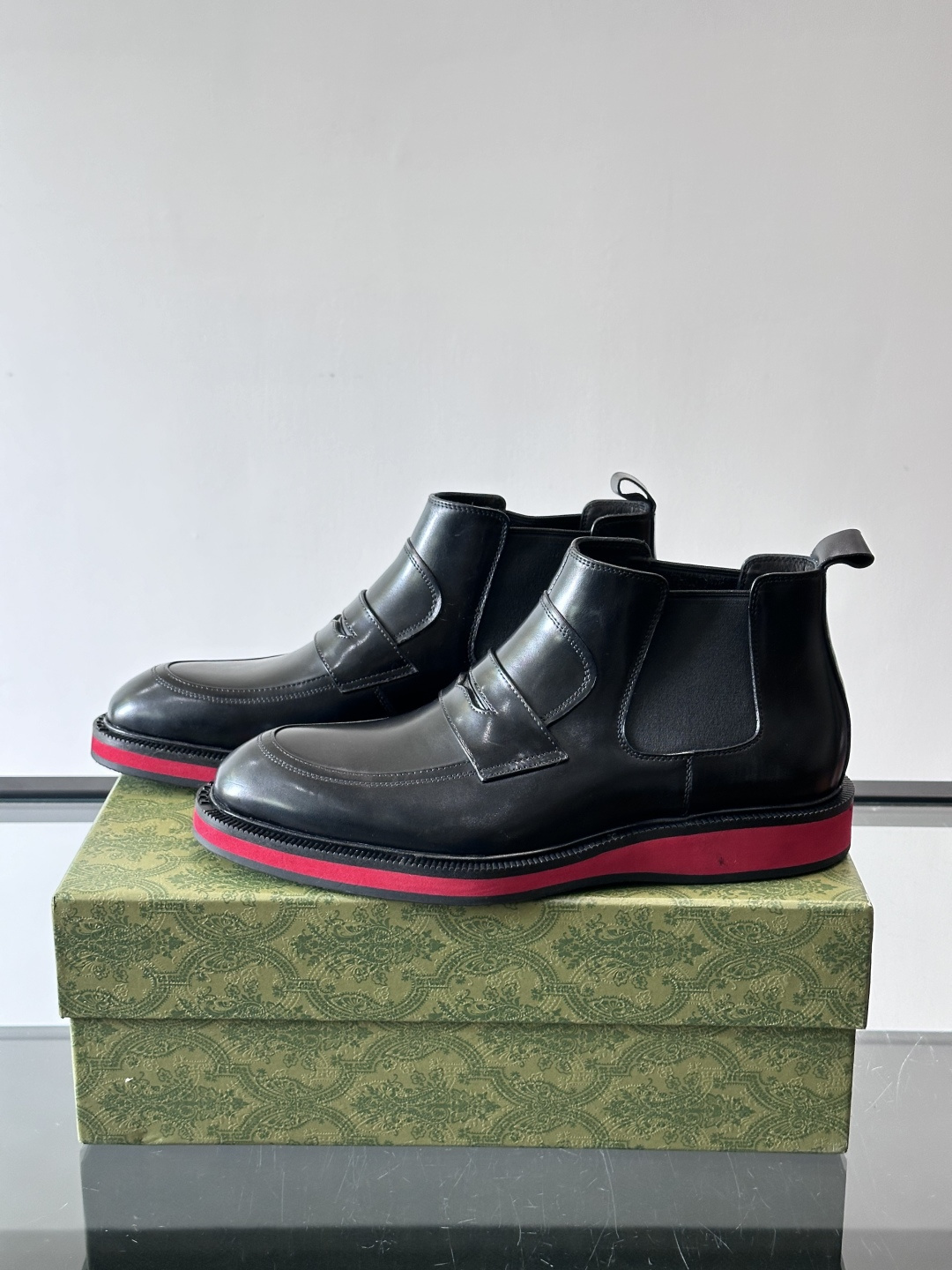 Gucci经典的拼色切尔西靴，采用高光泽黑色皮革搭配标志性的红绿织带细节，鞋底为亮眼的红色，整体设计兼具