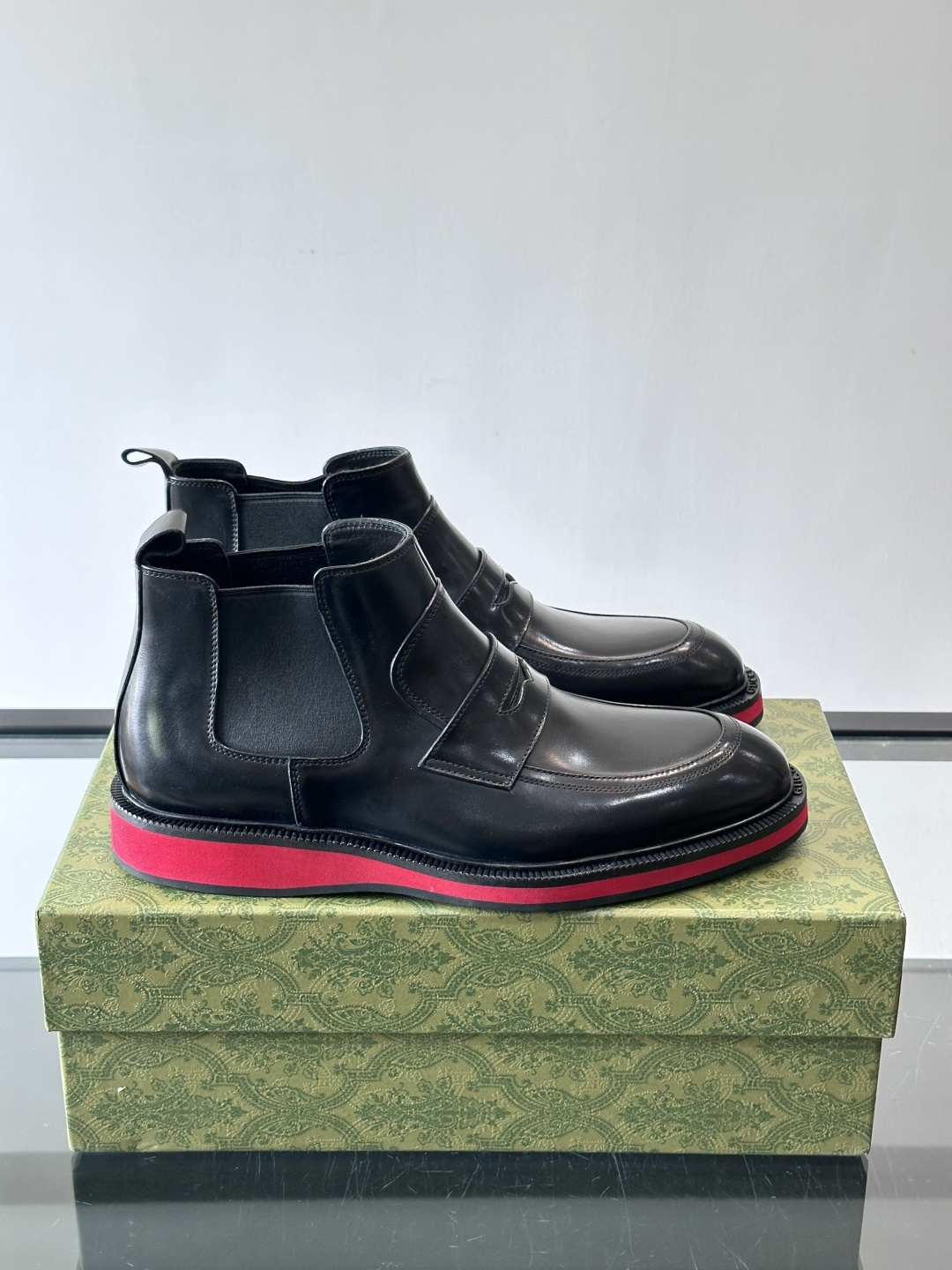 Gucci经典的拼色切尔西靴，采用高光泽黑色皮革搭配标志性的红绿织带细节，鞋底为亮眼的红色，整体设计兼具