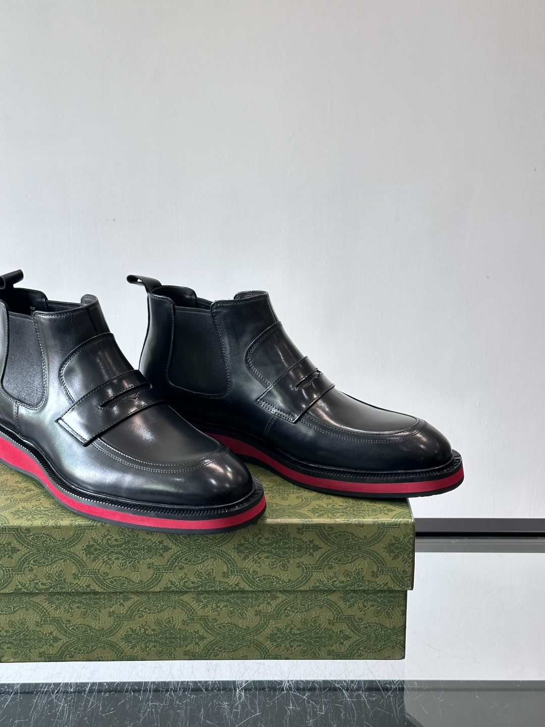 Gucci经典的拼色切尔西靴，采用高光泽黑色皮革搭配标志性的红绿织带细节，鞋底为亮眼的红色，整体设计兼具