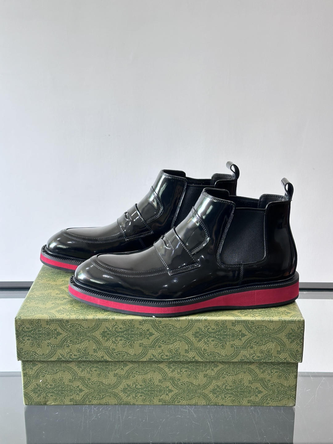 Gucci经典的拼色切尔西靴，采用高光泽黑色皮革搭配标志性的红绿织带细节，鞋底为亮眼的红色，整体设计兼具