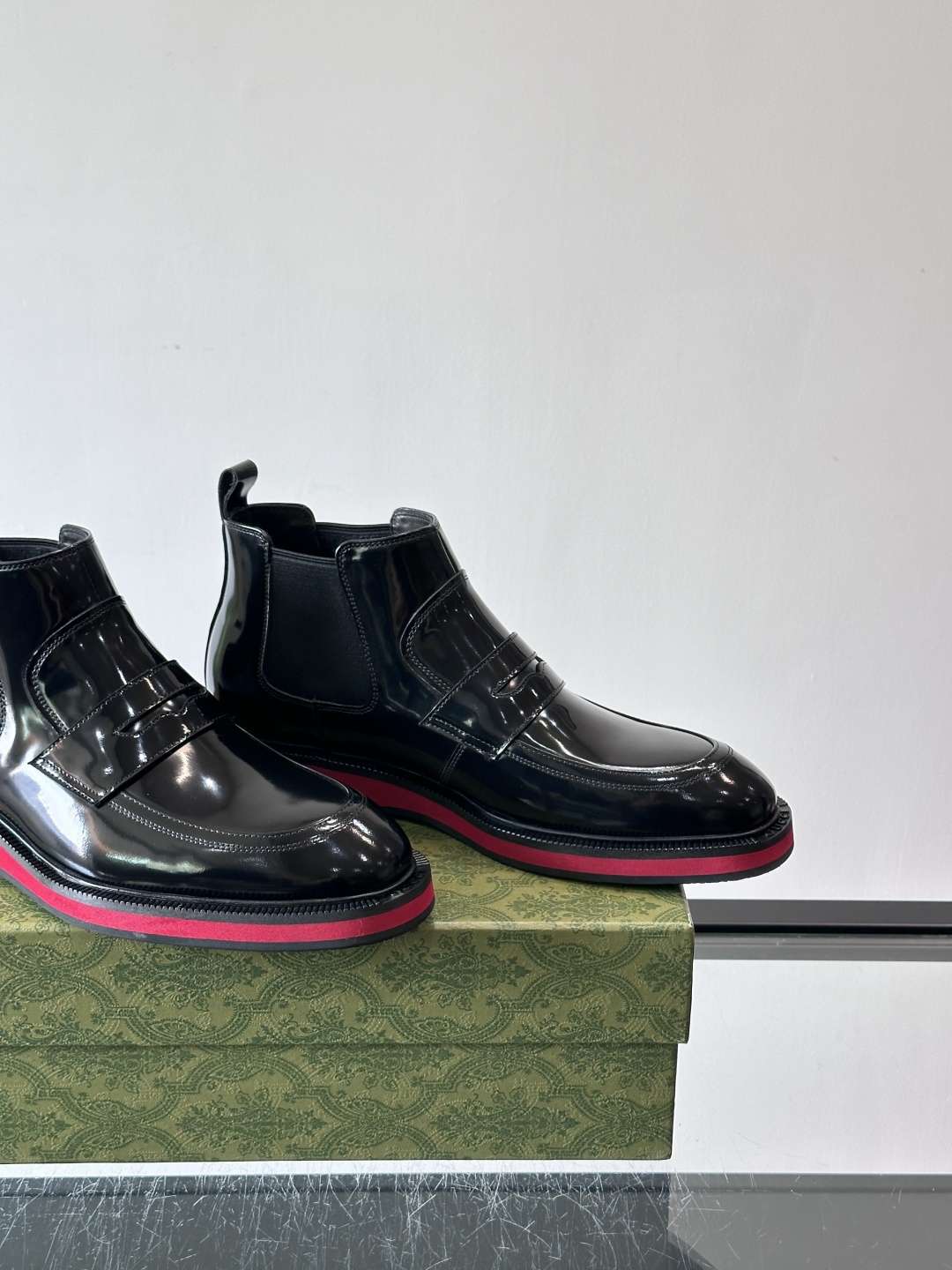 Gucci经典的拼色切尔西靴，采用高光泽黑色皮革搭配标志性的红绿织带细节，鞋底为亮眼的红色，整体设计兼具