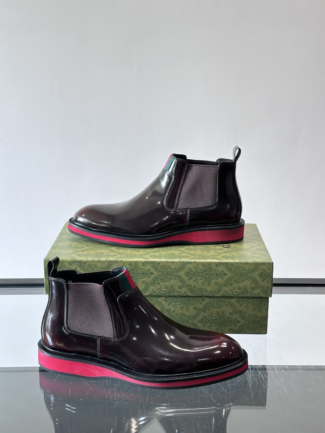 Gucci经典的拼色切尔西靴，采用高光泽黑色皮革搭配标志性的红绿织带细节，鞋底为亮眼的红色，整体设计兼具