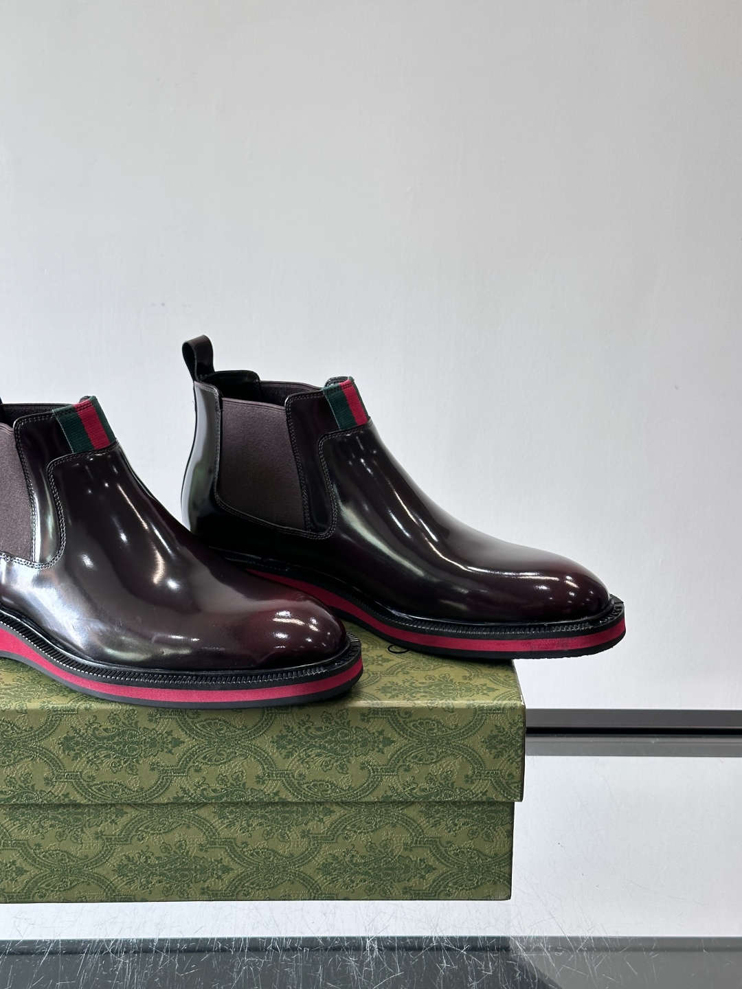 Gucci经典的拼色切尔西靴，采用高光泽黑色皮革搭配标志性的红绿织带细节，鞋底为亮眼的红色，整体设计兼具