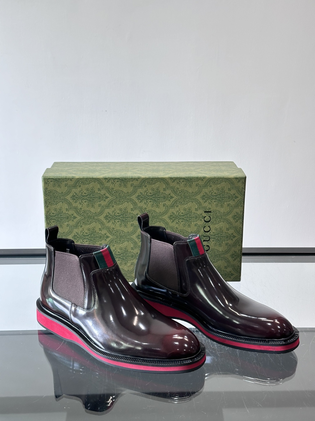 Gucci经典的拼色切尔西靴，采用高光泽黑色皮革搭配标志性的红绿织带细节，鞋底为亮眼的红色，整体设计兼具