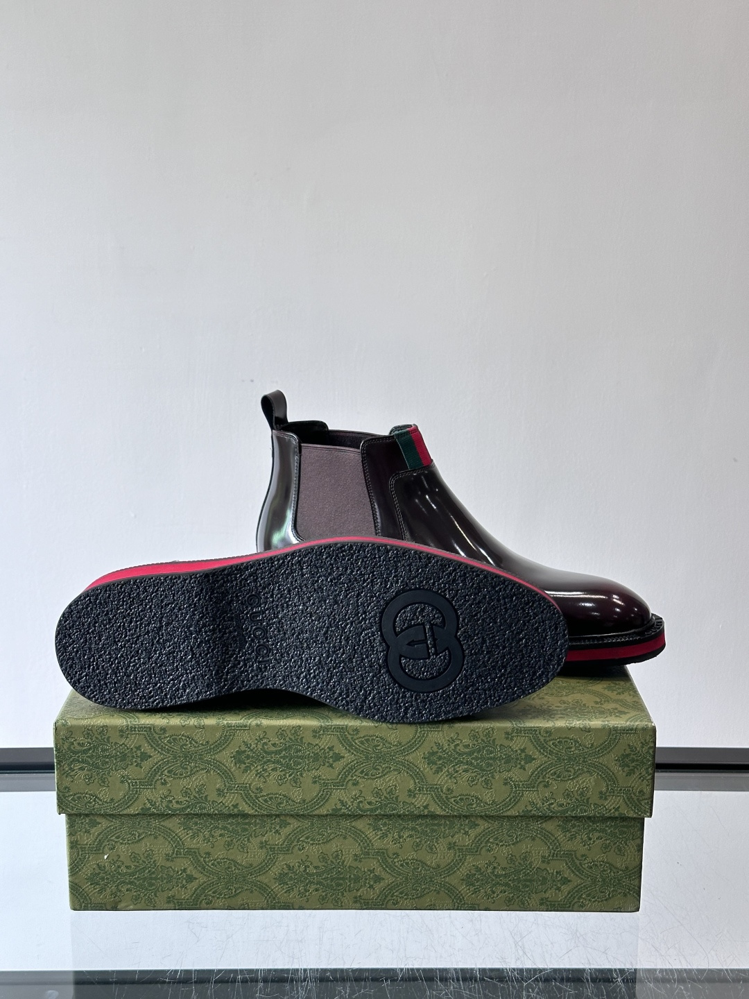 Gucci经典的拼色切尔西靴，采用高光泽黑色皮革搭配标志性的红绿织带细节，鞋底为亮眼的红色，整体设计兼具