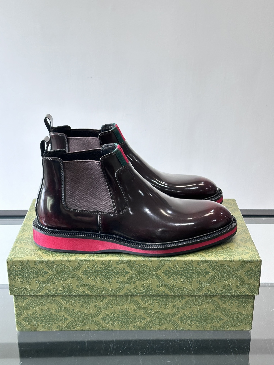 Gucci经典的拼色切尔西靴，采用高光泽黑色皮革搭配标志性的红绿织带细节，鞋底为亮眼的红色，整体设计兼具