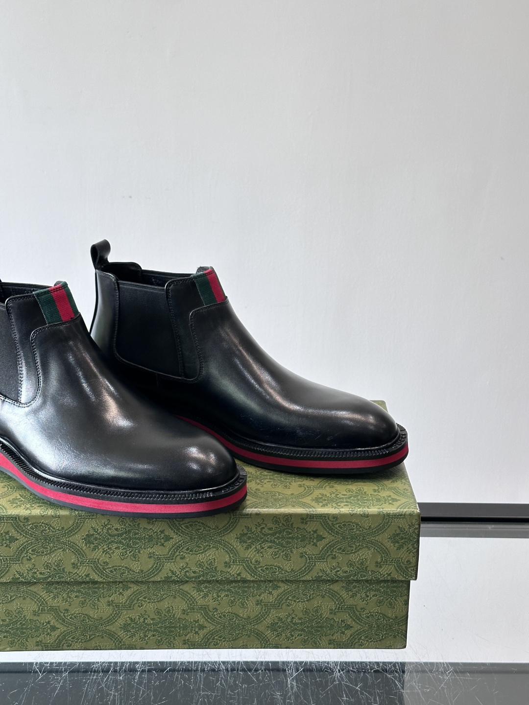 Gucci经典的拼色切尔西靴，采用高光泽黑色皮革搭配标志性的红绿织带细节，鞋底为亮眼的红色，整体设计兼具