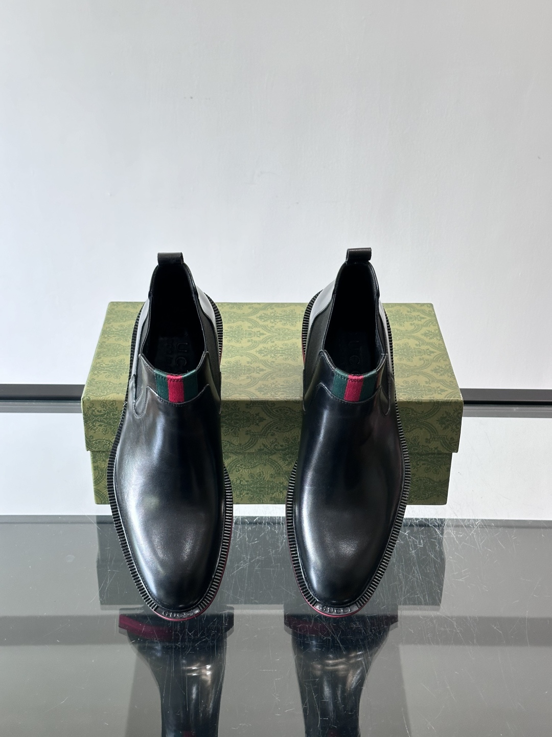 Gucci经典的拼色切尔西靴，采用高光泽黑色皮革搭配标志性的红绿织带细节，鞋底为亮眼的红色，整体设计兼具