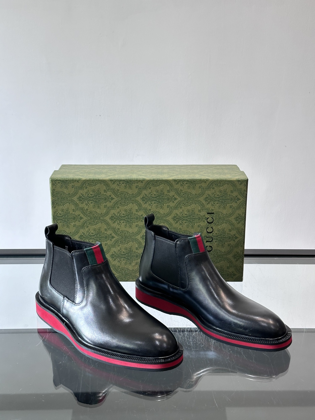 Gucci经典的拼色切尔西靴，采用高光泽黑色皮革搭配标志性的红绿织带细节，鞋底为亮眼的红色，整体设计兼具