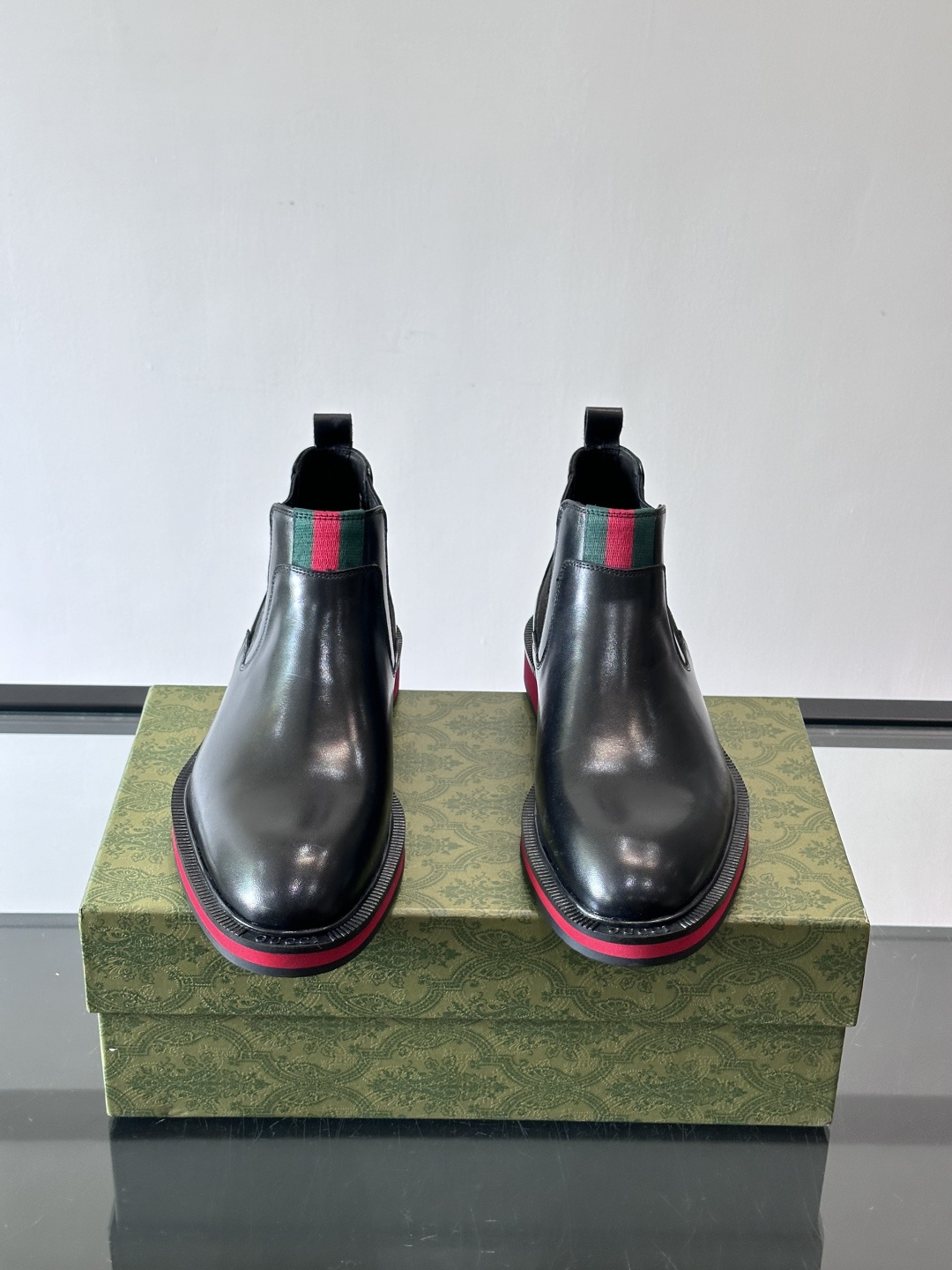 Gucci经典的拼色切尔西靴，采用高光泽黑色皮革搭配标志性的红绿织带细节，鞋底为亮眼的红色，整体设计兼具