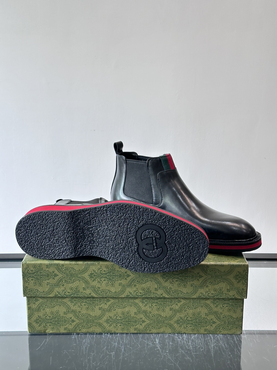 Gucci经典的拼色切尔西靴，采用高光泽黑色皮革搭配标志性的红绿织带细节，鞋底为亮眼的红色，整体设计兼具