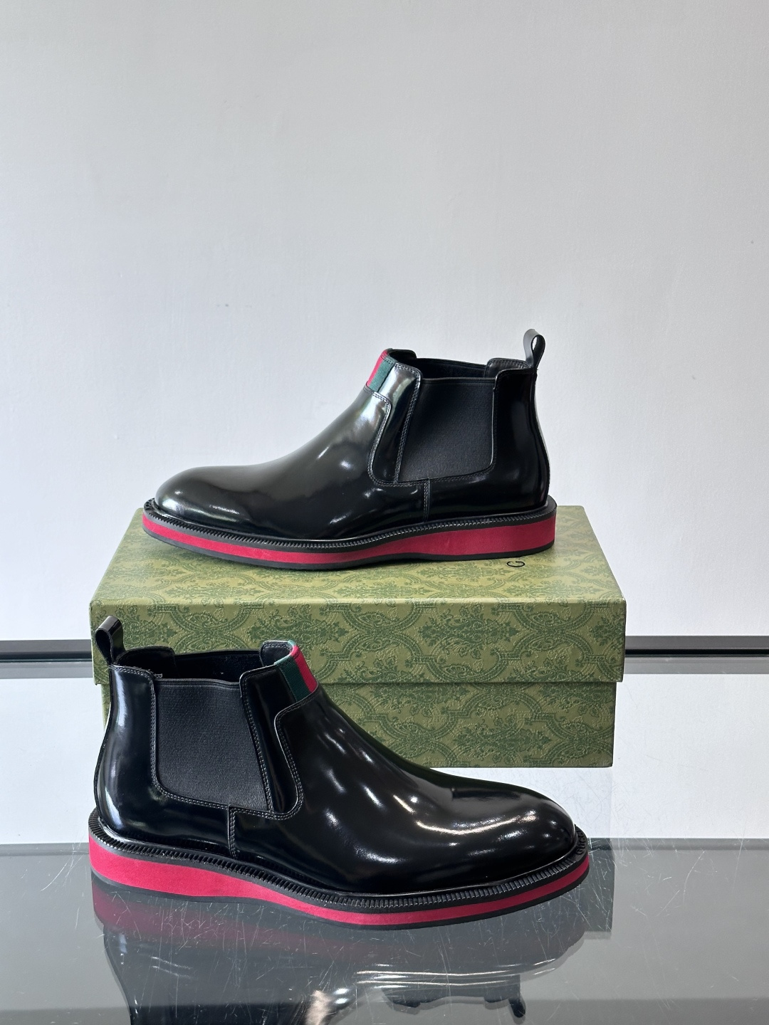 Gucci经典的拼色切尔西靴，采用高光泽黑色皮革搭配标志性的红绿织带细节，鞋底为亮眼的红色，整体设计兼具
