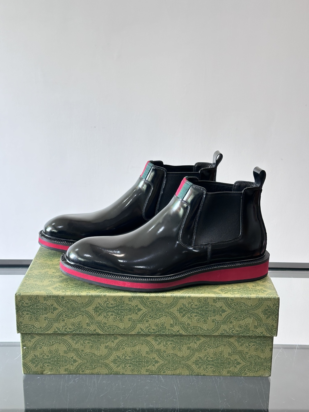 Gucci经典的拼色切尔西靴，采用高光泽黑色皮革搭配标志性的红绿织带细节，鞋底为亮眼的红色，整体设计兼具