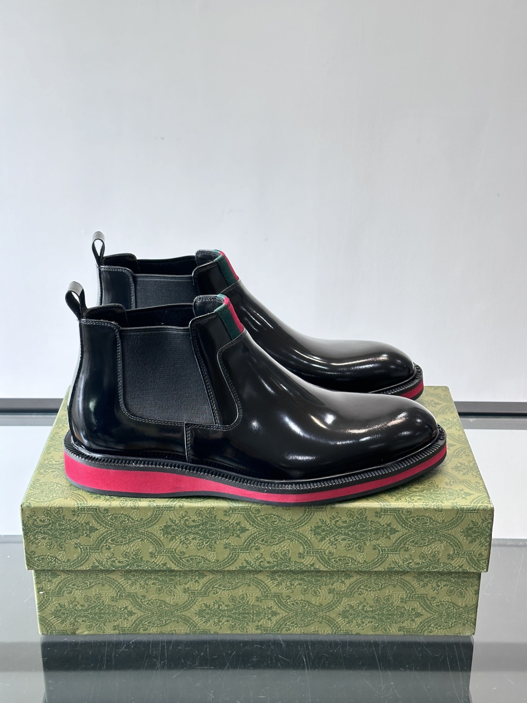 Gucci经典的拼色切尔西靴，采用高光泽黑色皮革搭配标志性的红绿织带细节，鞋底为亮眼的红色，整体设计兼具
