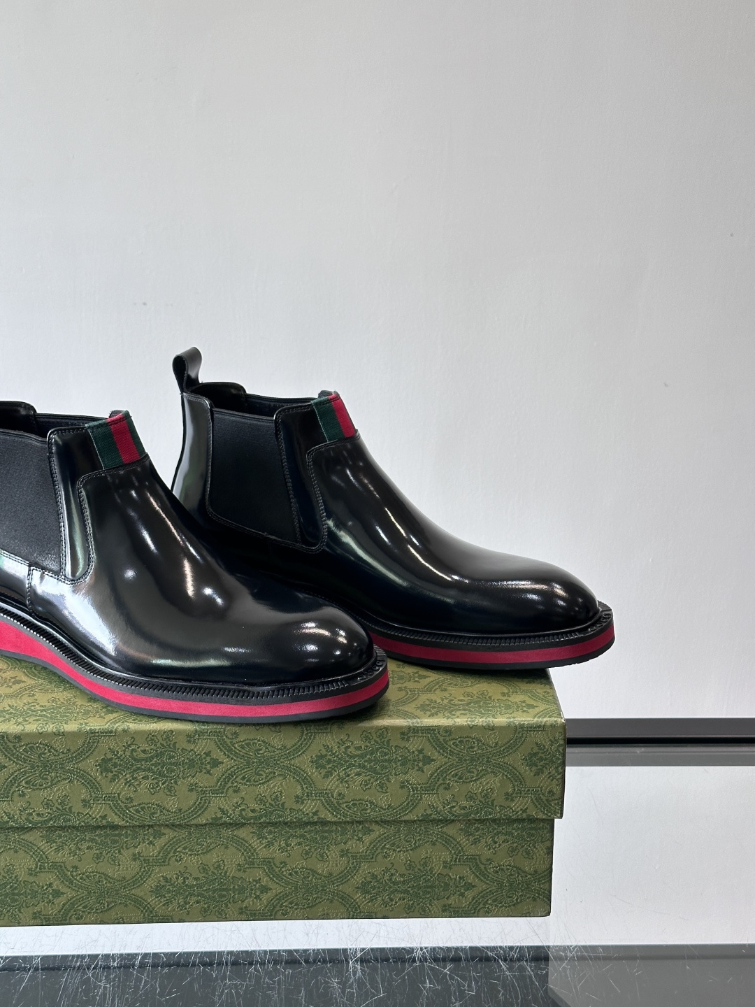 Gucci经典的拼色切尔西靴，采用高光泽黑色皮革搭配标志性的红绿织带细节，鞋底为亮眼的红色，整体设计兼具