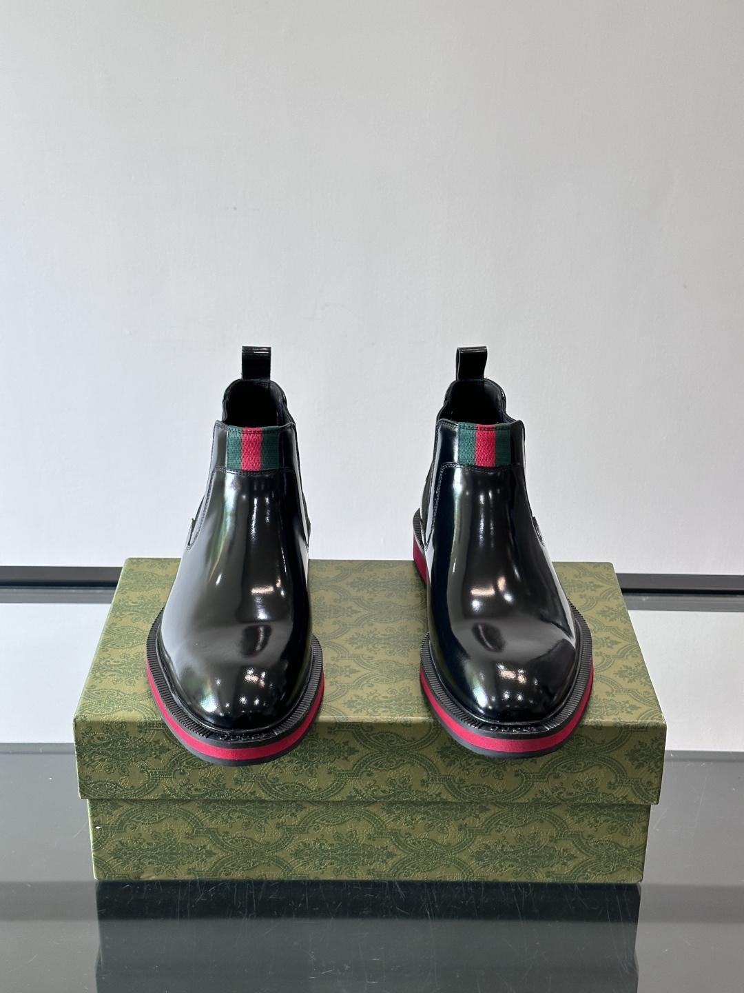 Gucci经典的拼色切尔西靴，采用高光泽黑色皮革搭配标志性的红绿织带细节，鞋底为亮眼的红色，整体设计兼具