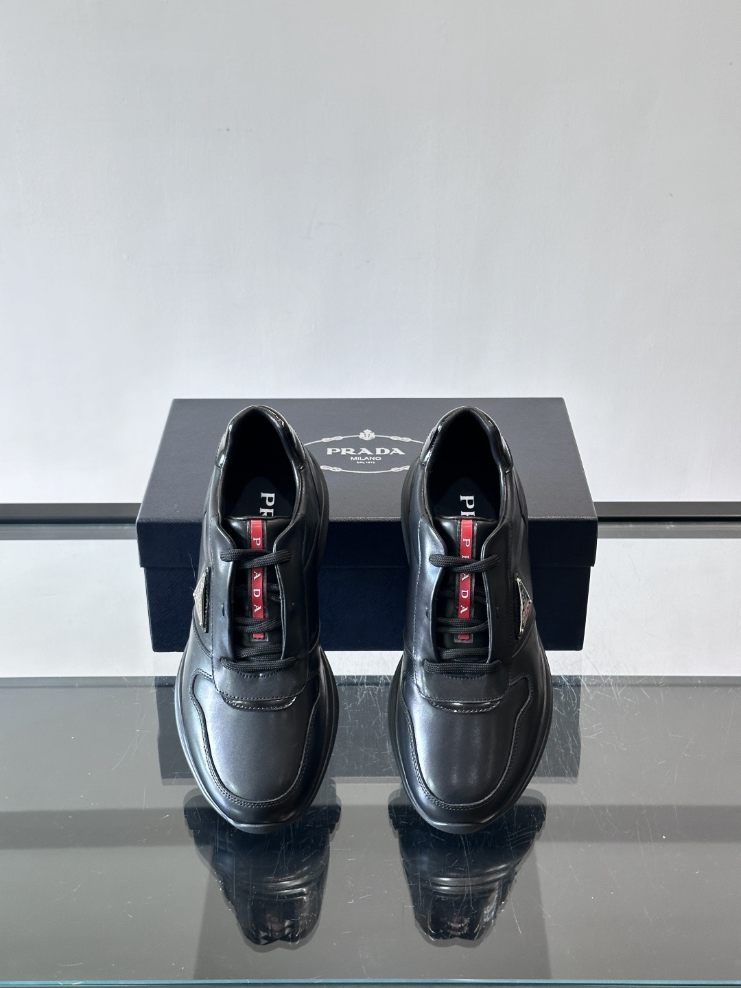 Prada黑色皮革运动鞋是品牌经典复古系列中的代表作，采用光滑小牛皮材质，搭配厚实橡胶大底和标志性的三角