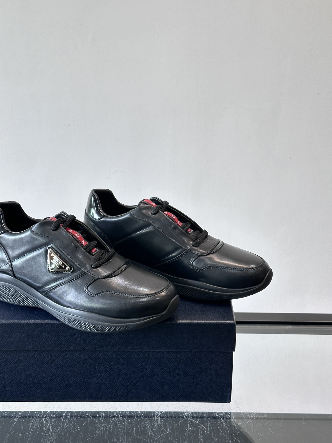 Prada黑色皮革运动鞋是品牌经典复古系列中的代表作，采用光滑小牛皮材质，搭配厚实橡胶大底和标志性的三角