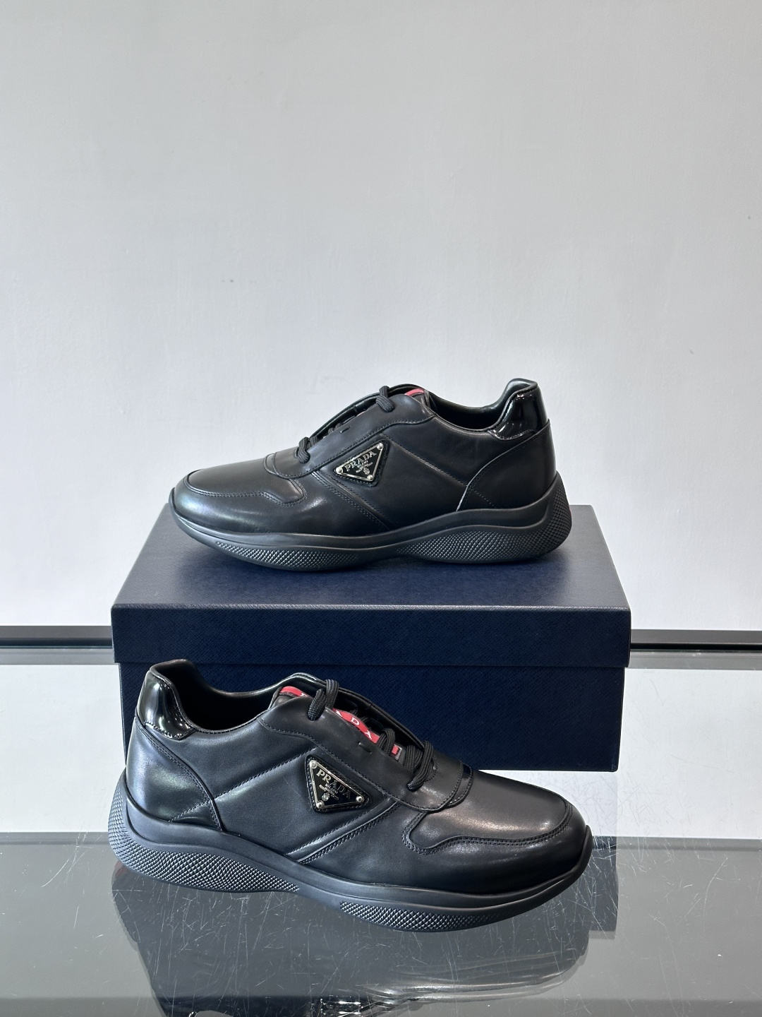 Prada黑色皮革运动鞋是品牌经典复古系列中的代表作，采用光滑小牛皮材质，搭配厚实橡胶大底和标志性的三角