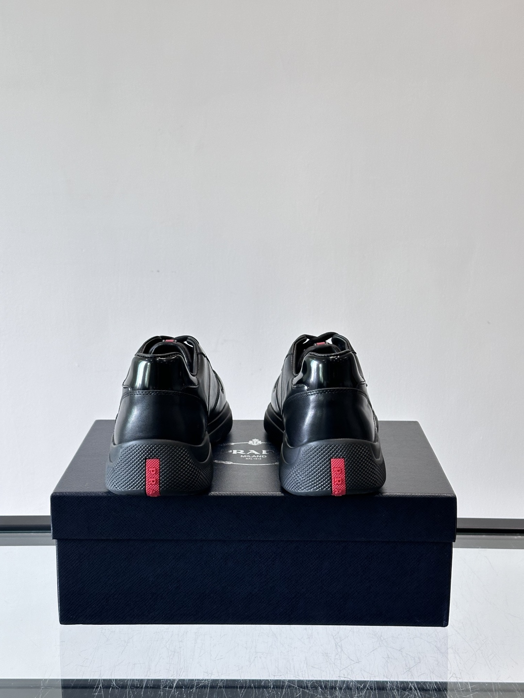 Prada黑色皮革运动鞋是品牌经典复古系列中的代表作，采用光滑小牛皮材质，搭配厚实橡胶大底和标志性的三角