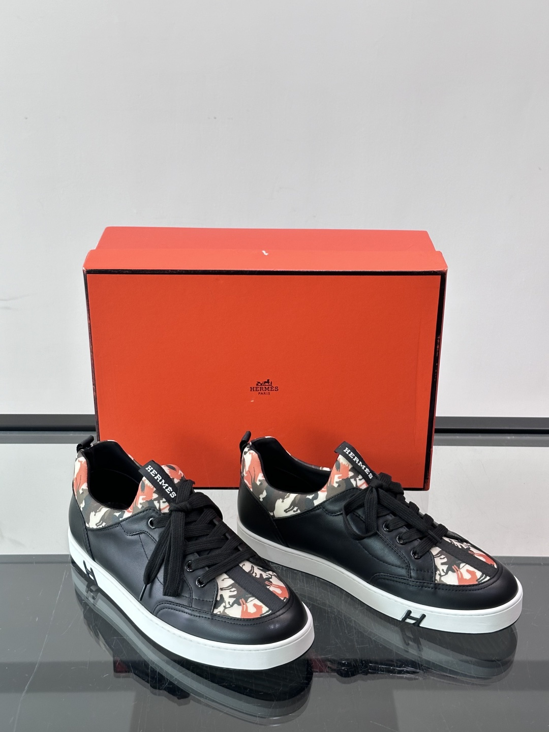 Hermès "Jungle" 迷彩板鞋​​，皮革鞋面搭配迷彩拼接，黑色鞋带和鞋舌"HERMES"字样，白色厚底。这双白