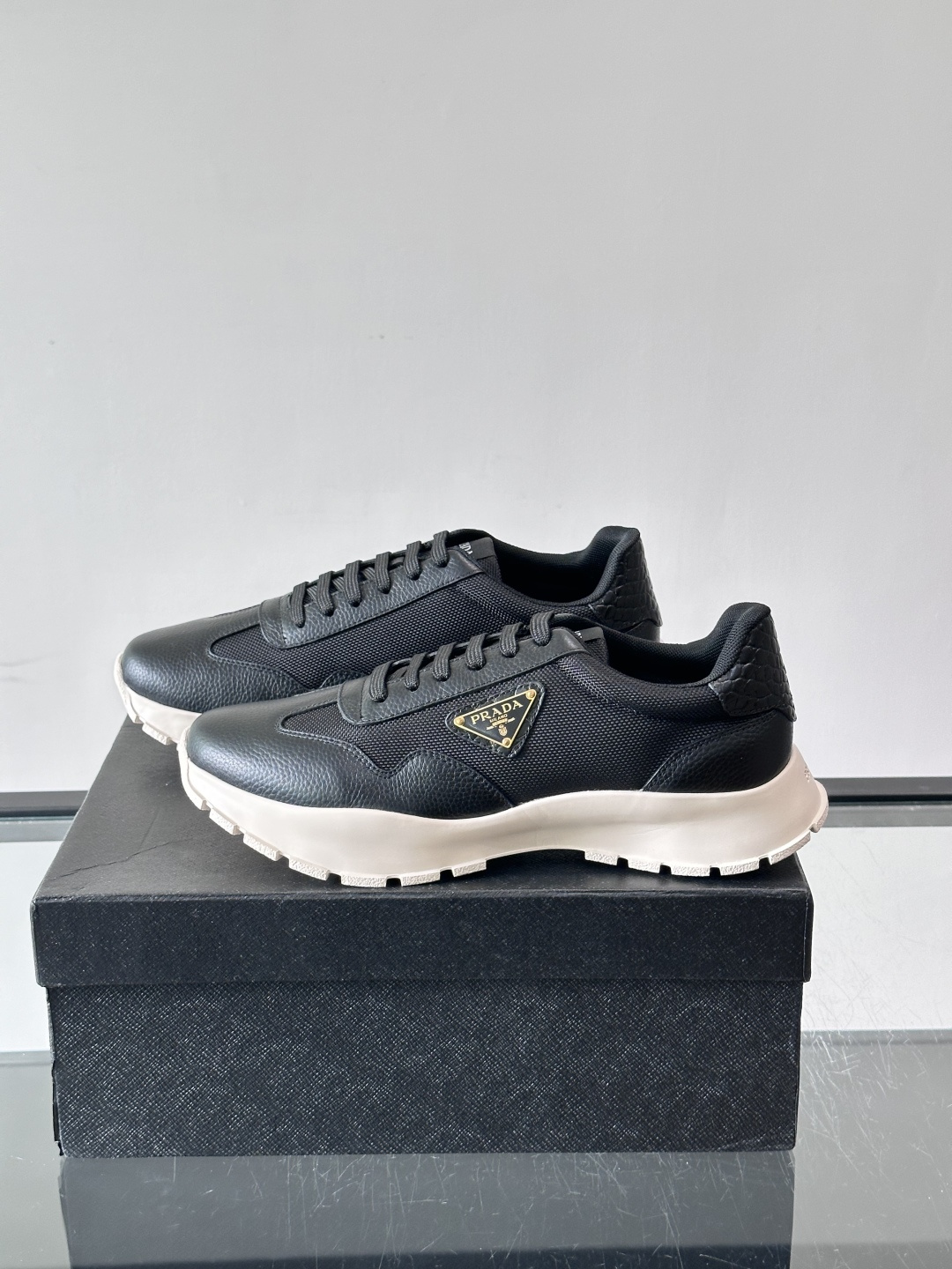 Prada 男士运动鞋,鞋面是荔枝纹皮革 + 网面拼接,鞋侧有金色三角形 Prada 徽标,质感上荔枝纹皮革的颗 Prada 男士运动鞋,鞋面是荔枝纹皮革 + 网面拼接,鞋侧有金色三角形 Prada 徽标,质感上荔枝纹皮革的颗