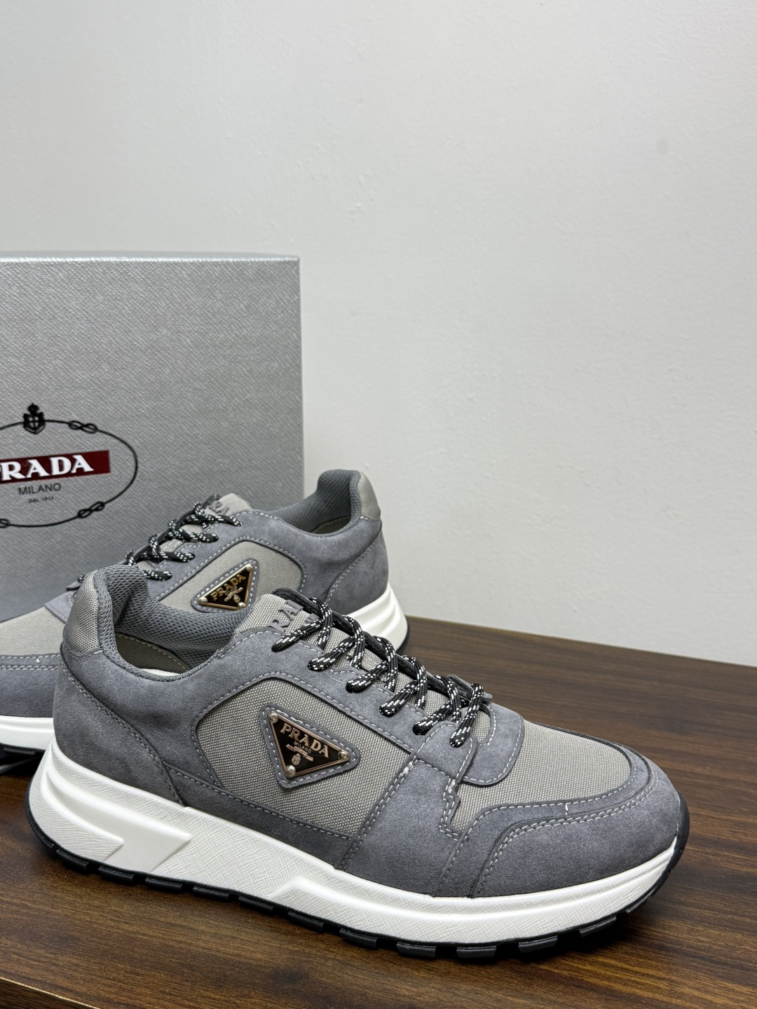 Prada Brush 运动鞋​​，鞋面是麂皮 + 尼龙织物拼接，侧面有 Prada 标志性的 三角珐琅金属标 ，厚底橡