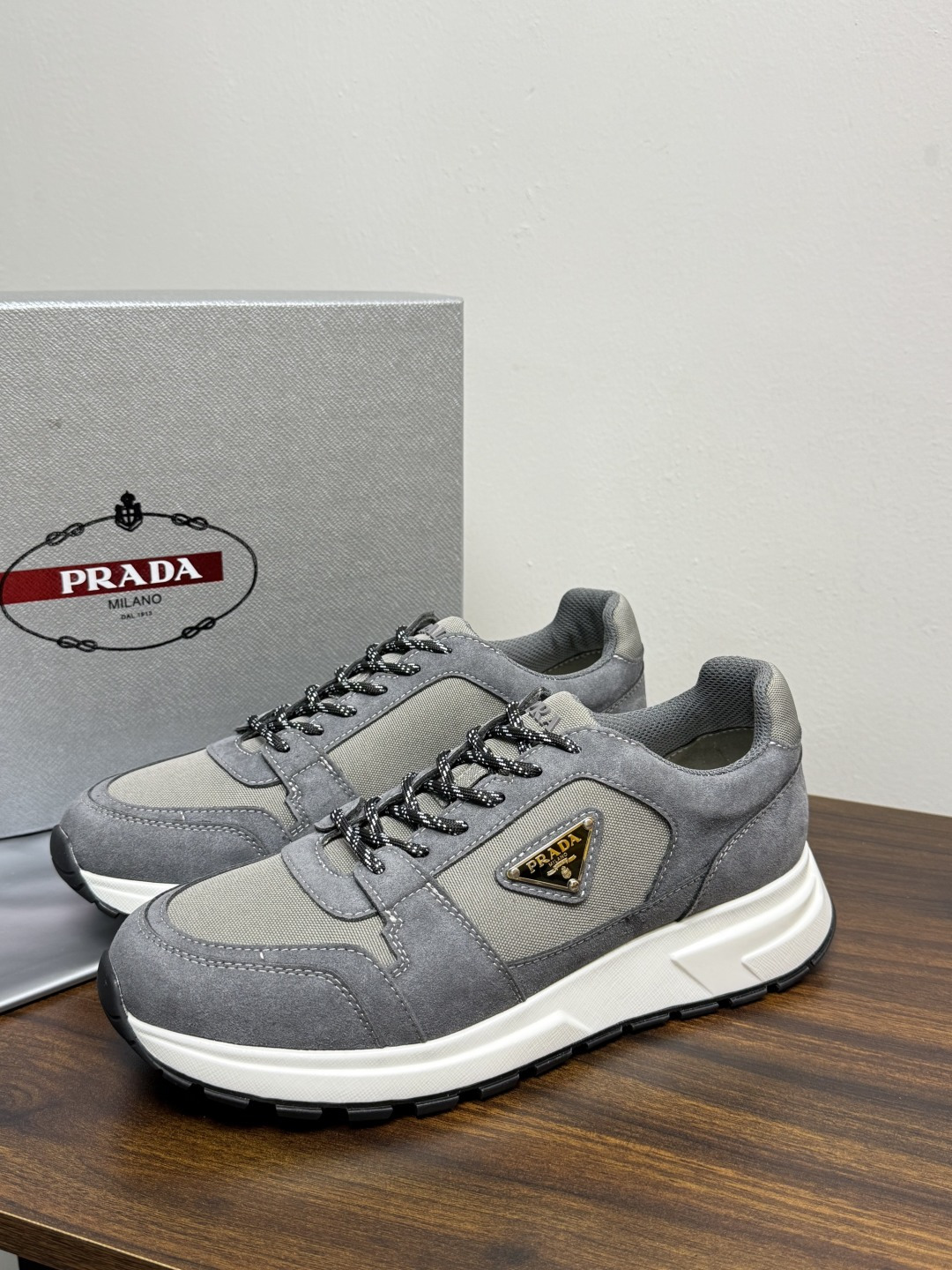 Prada Brush 运动鞋​​，鞋面是麂皮 + 尼龙织物拼接，侧面有 Prada 标志性的 三角珐琅金属标 ，厚底橡