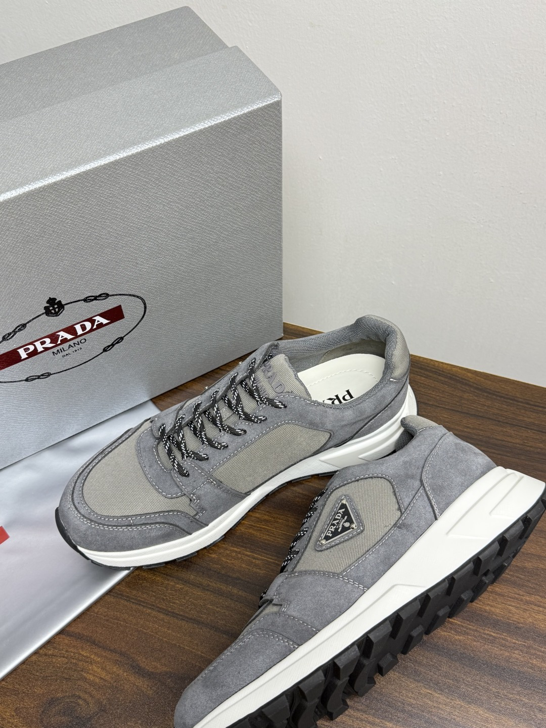 Prada Brush 运动鞋​​，鞋面是麂皮 + 尼龙织物拼接，侧面有 Prada 标志性的 三角珐琅金属标 ，厚底橡