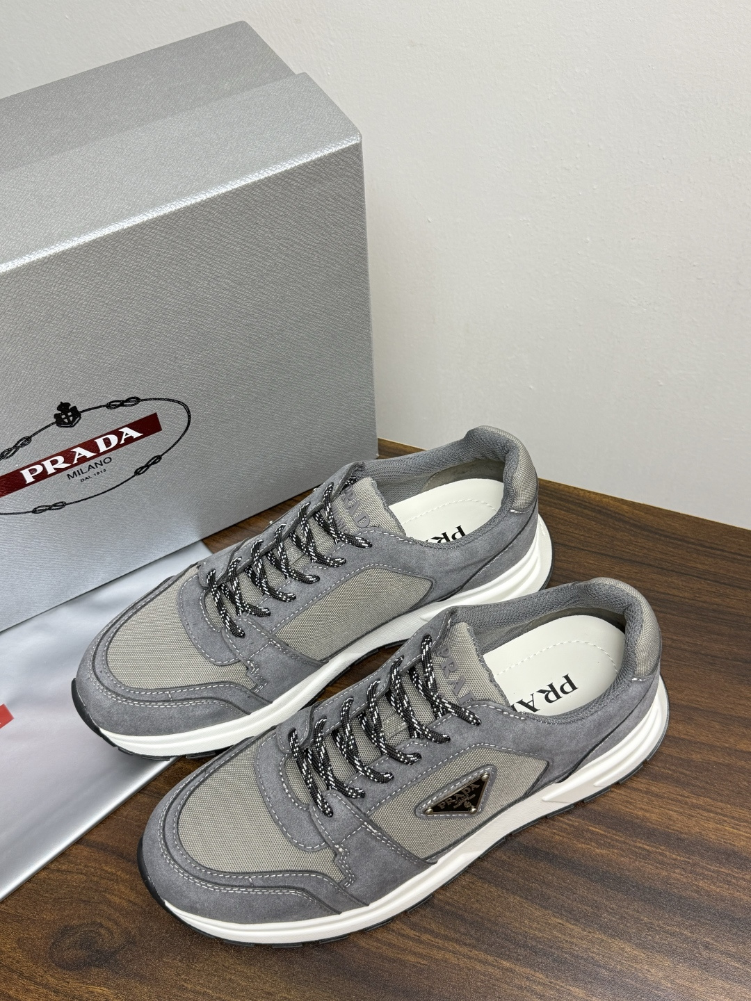 Prada Brush 运动鞋​​，鞋面是麂皮 + 尼龙织物拼接，侧面有 Prada 标志性的 三角珐琅金属标 ，厚底橡
