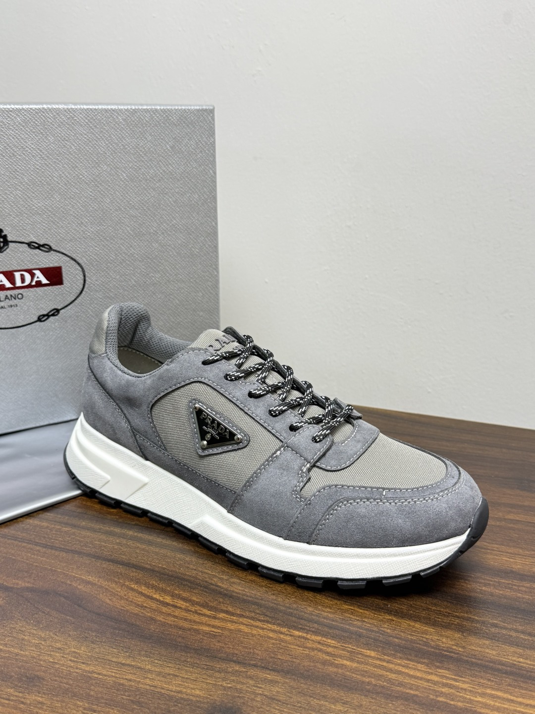 Prada Brush 运动鞋​​，鞋面是麂皮 + 尼龙织物拼接，侧面有 Prada 标志性的 三角珐琅金属标 ，厚底橡