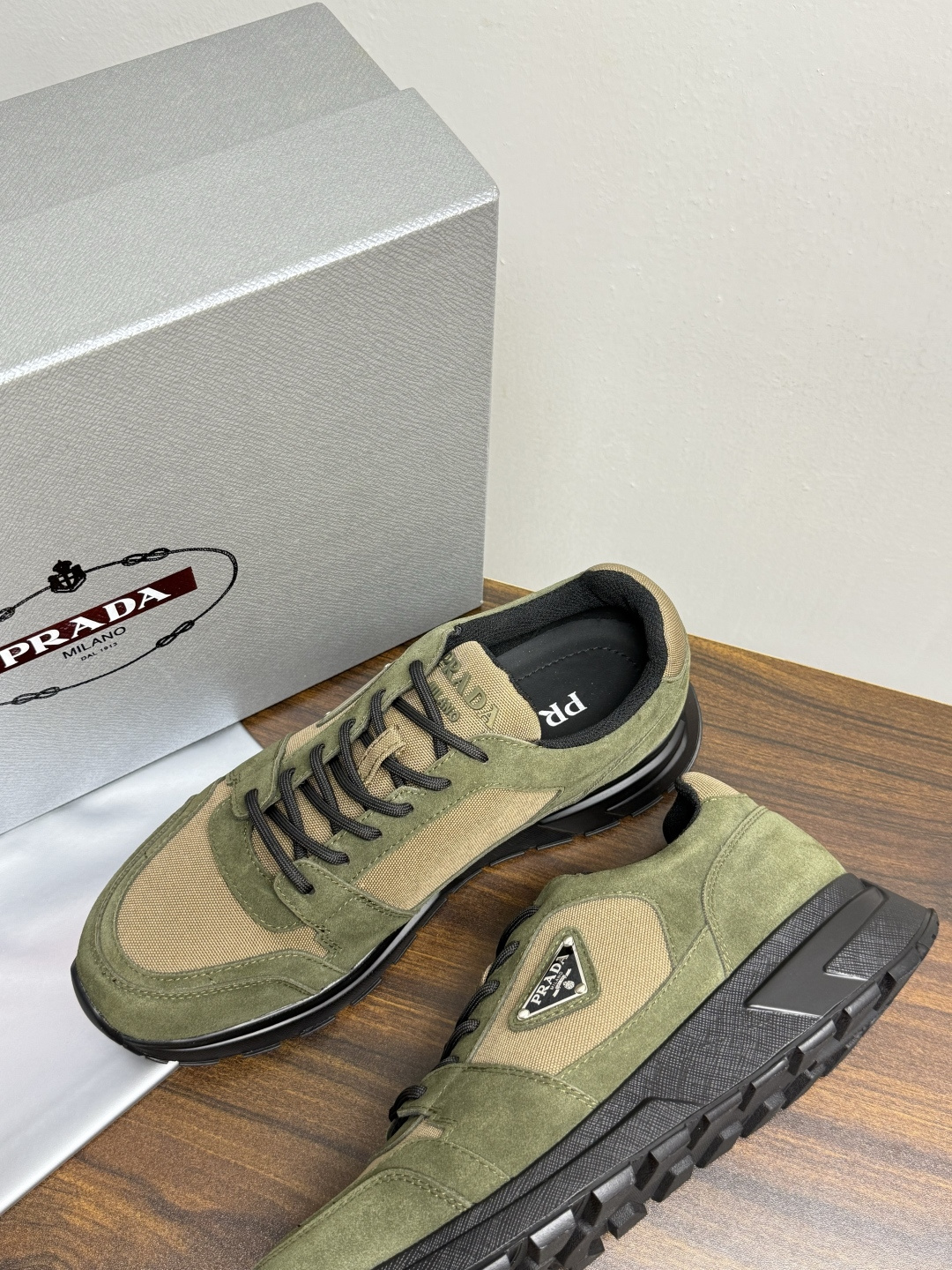 Prada Brush 运动鞋​​，鞋面是麂皮 + 尼龙织物拼接，侧面有 Prada 标志性的 三角珐琅金属标 ，厚底橡
