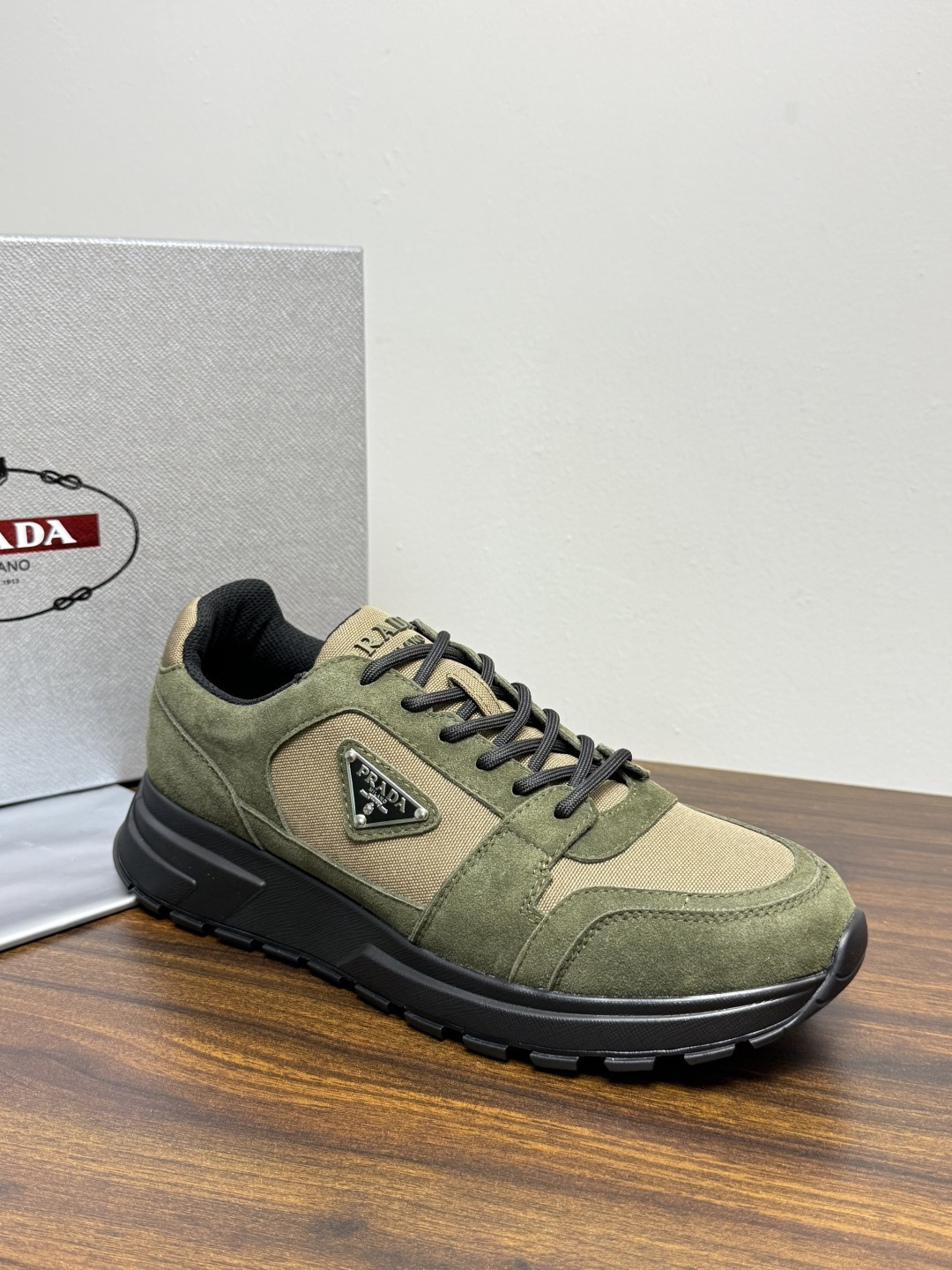 Prada Brush 运动鞋​​，鞋面是麂皮 + 尼龙织物拼接，侧面有 Prada 标志性的 三角珐琅金属标 ，厚底橡