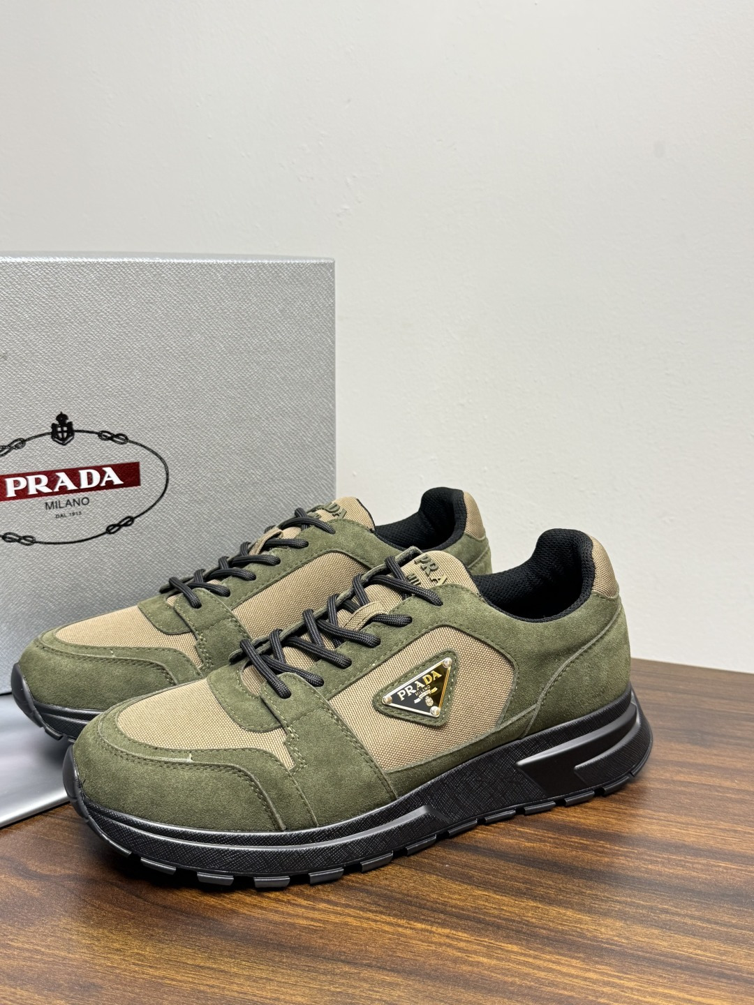 Prada Brush 运动鞋​​，鞋面是麂皮 + 尼龙织物拼接，侧面有 Prada 标志性的 三角珐琅金属标 ，厚底橡
