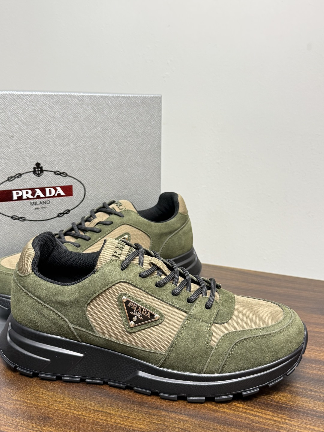 Prada Brush 运动鞋​​，鞋面是麂皮 + 尼龙织物拼接，侧面有 Prada 标志性的 三角珐琅金属标 ，厚底橡