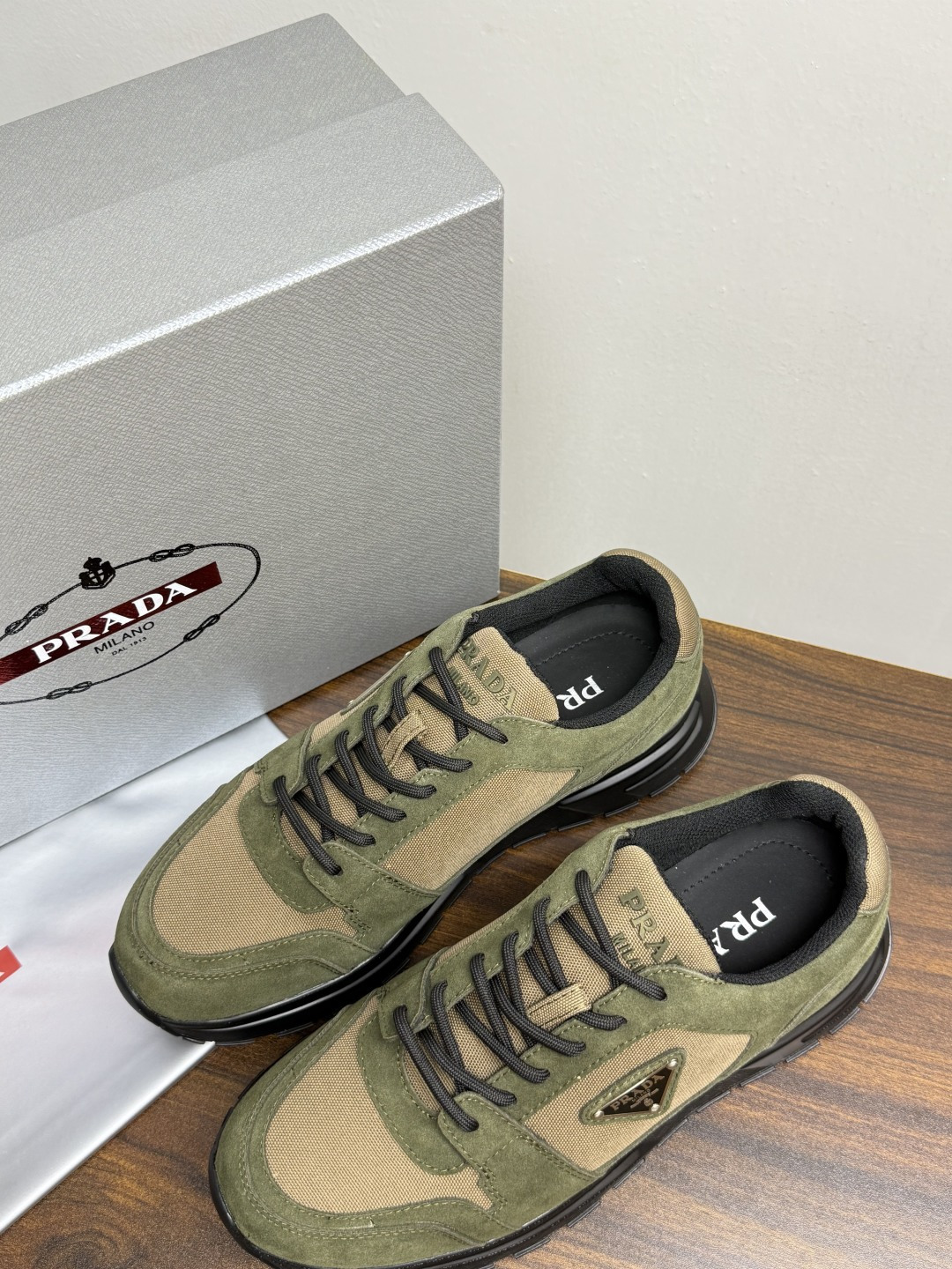 Prada Brush 运动鞋​​，鞋面是麂皮 + 尼龙织物拼接，侧面有 Prada 标志性的 三角珐琅金属标 ，厚底橡