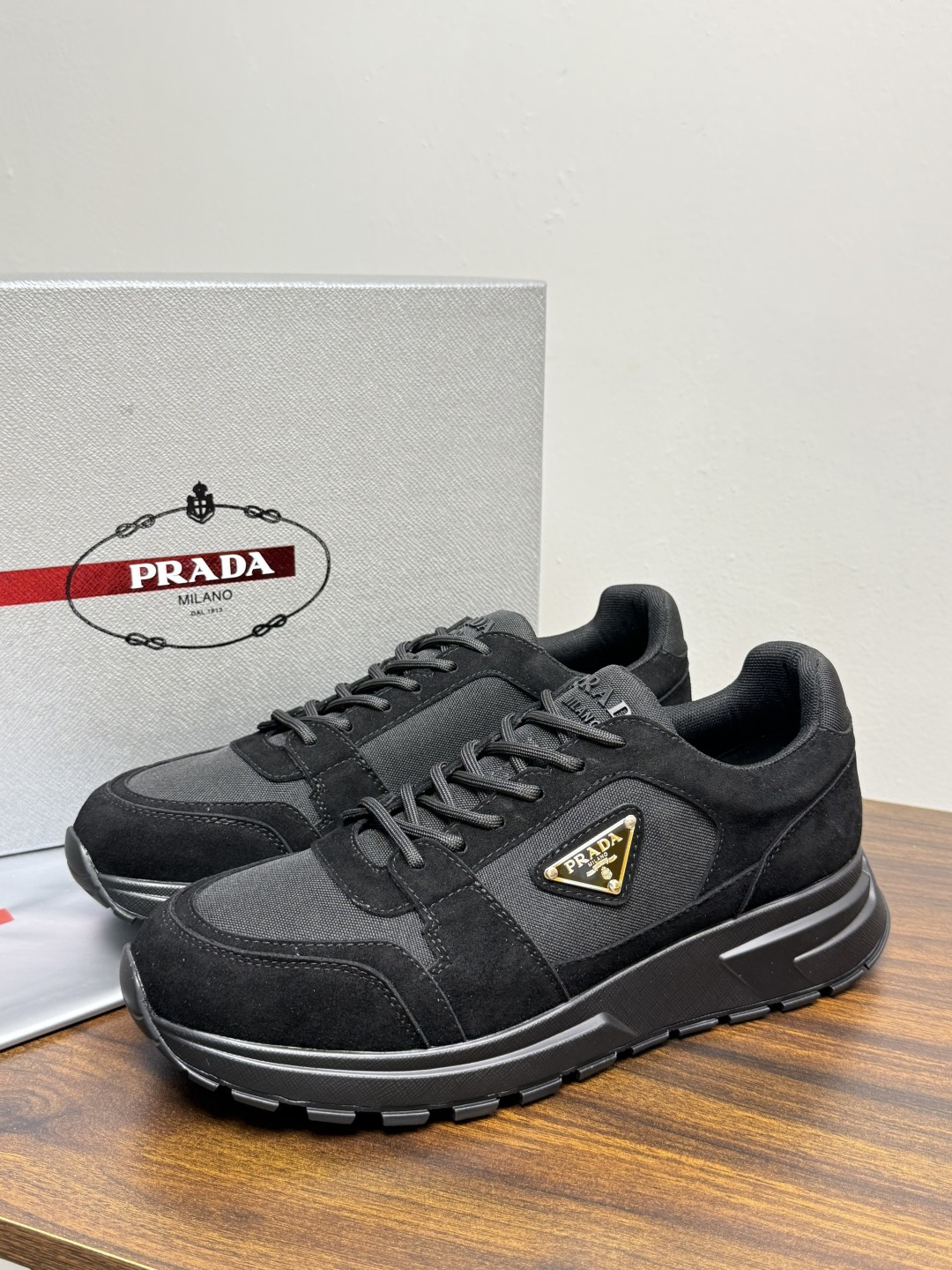 Prada Brush 运动鞋​​，鞋面是麂皮 + 尼龙织物拼接，侧面有 Prada 标志性的 三角珐琅金属标 ，厚底橡
