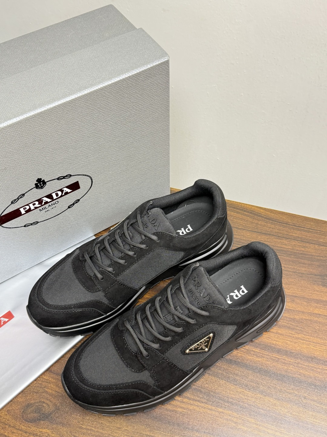 Prada Brush 运动鞋​​，鞋面是麂皮 + 尼龙织物拼接，侧面有 Prada 标志性的 三角珐琅金属标 ，厚底橡