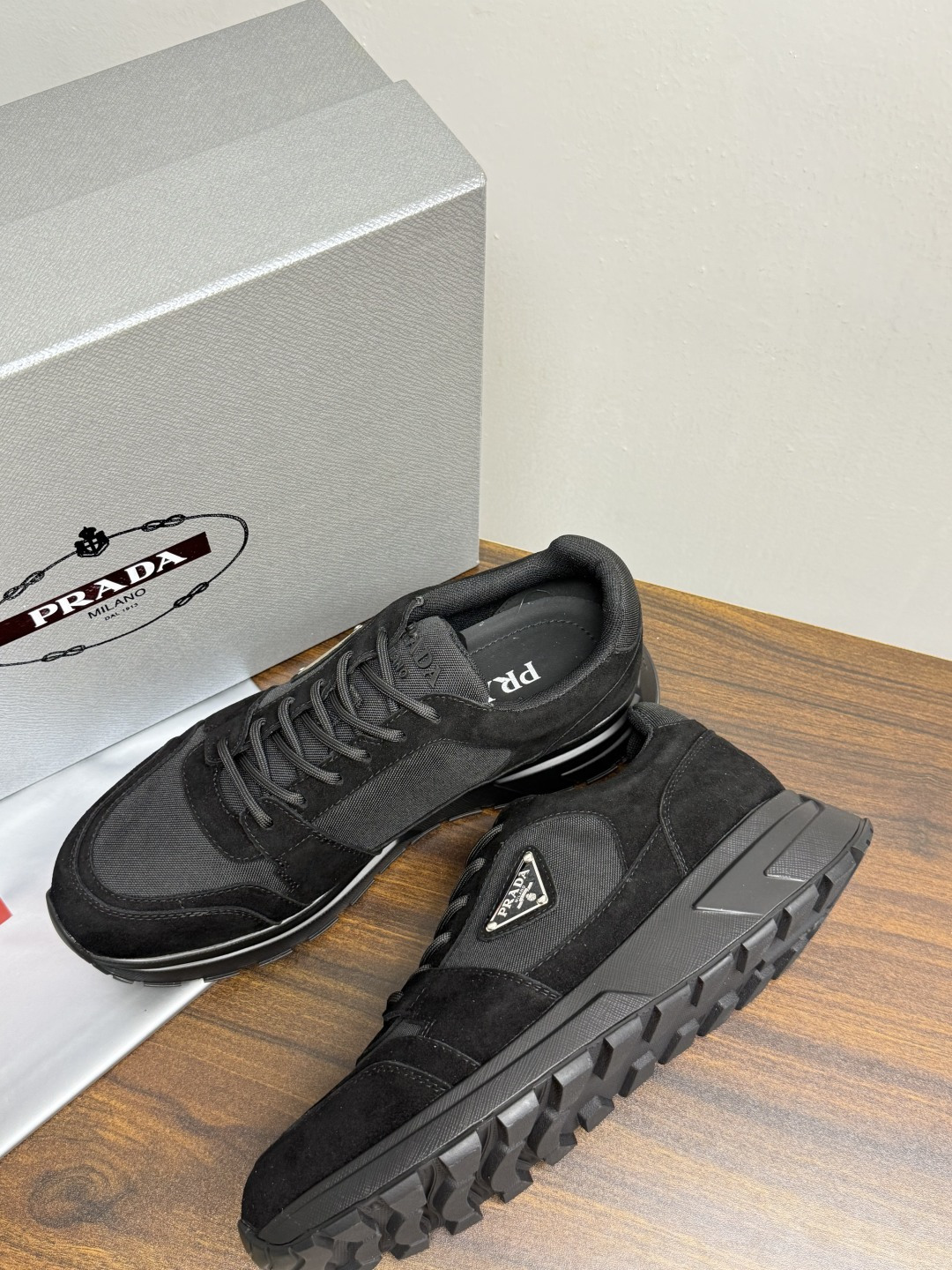Prada Brush 运动鞋​​，鞋面是麂皮 + 尼龙织物拼接，侧面有 Prada 标志性的 三角珐琅金属标 ，厚底橡