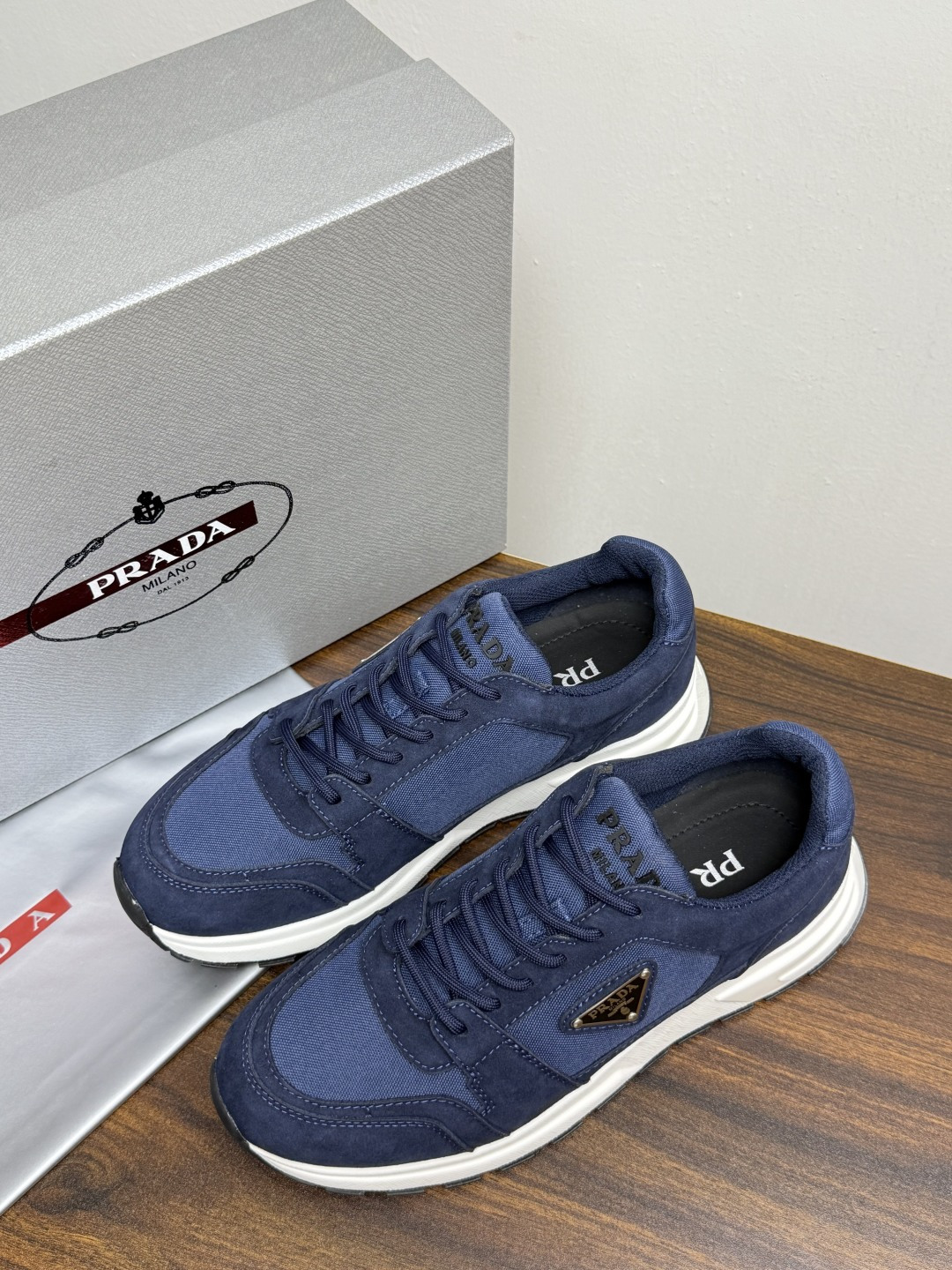 Prada Brush 运动鞋​​，鞋面是麂皮 + 尼龙织物拼接，侧面有 Prada 标志性的 三角珐琅金属标 ，厚底橡